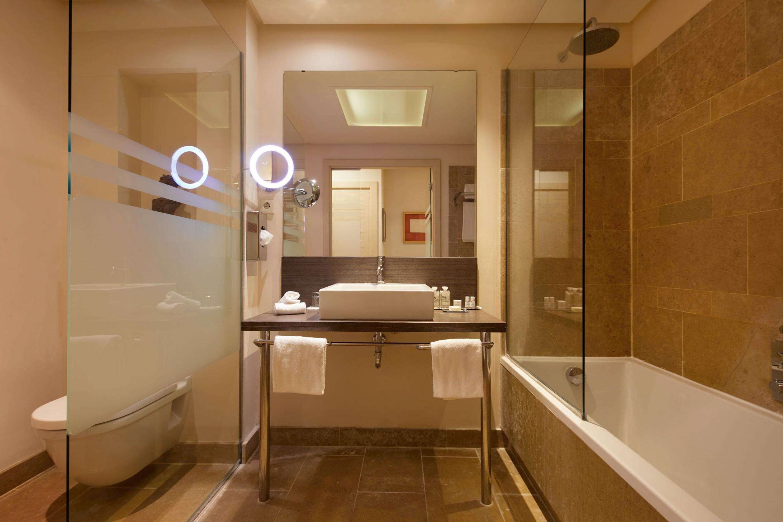 Un baño moderno con ducha de vidrio, un lavamanos blanco y un espejo grande.