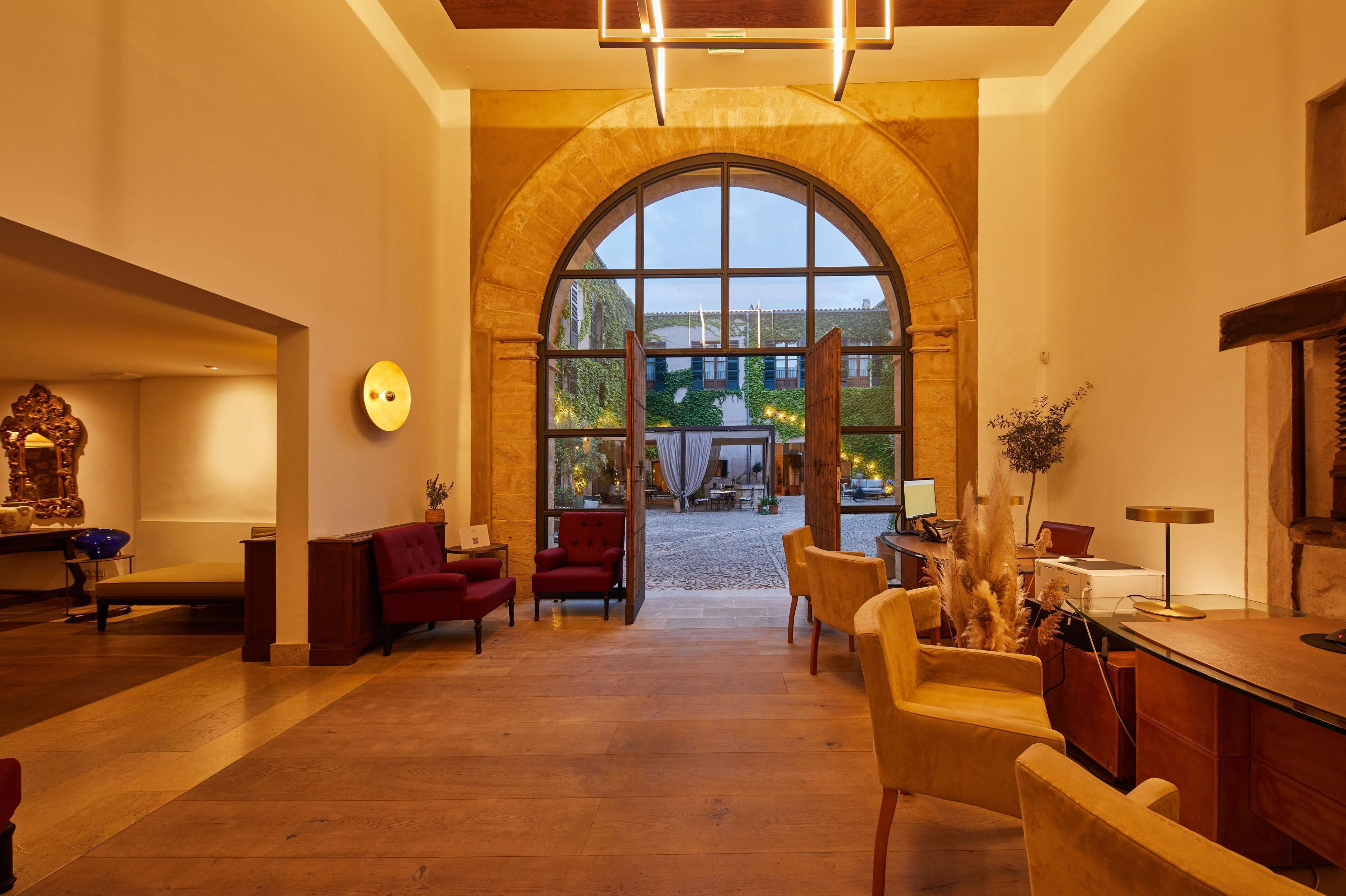 A spacious lobby with a large arched window, wooden flooring, and a mix of seating options including sofas and chairs.