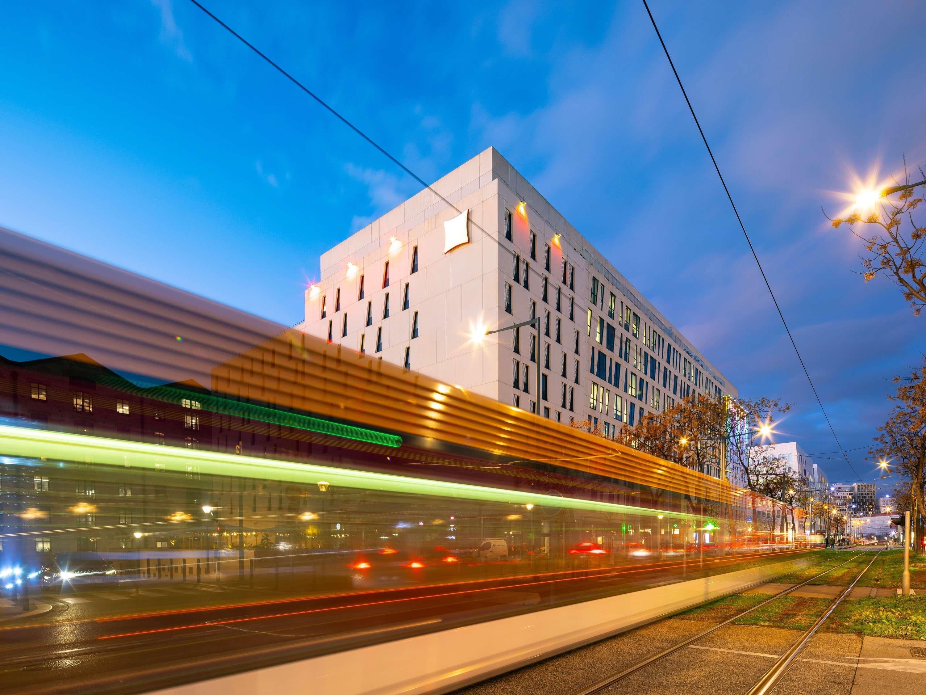 A modern building with a glass facade and a tram line passing by.