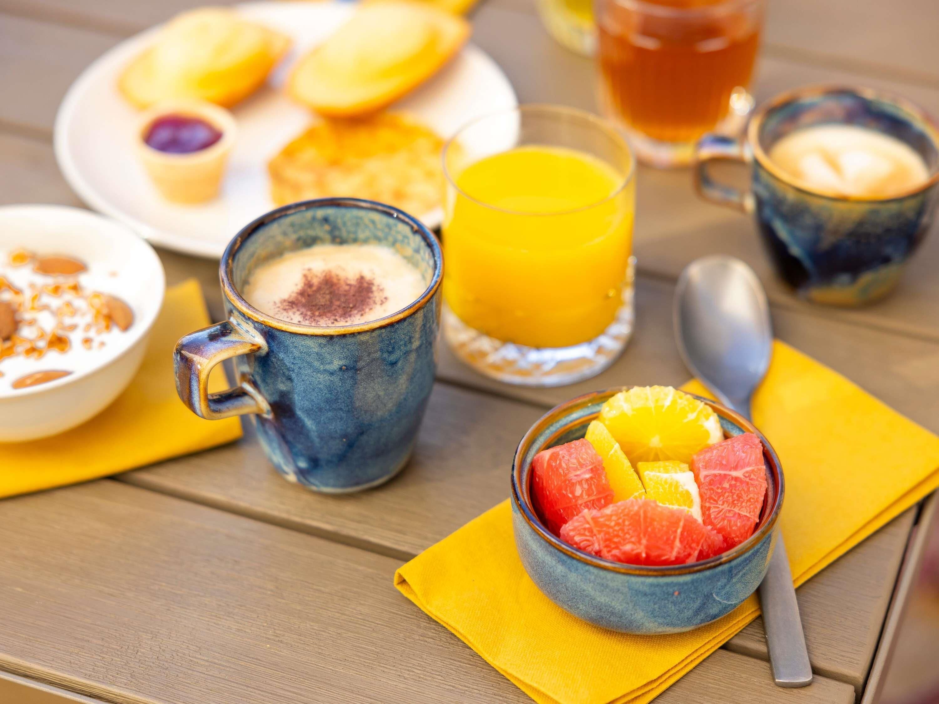 Desayuno con una taza, un bol de fruta y un vaso de zumo de naranja sobre una mesa de madera.