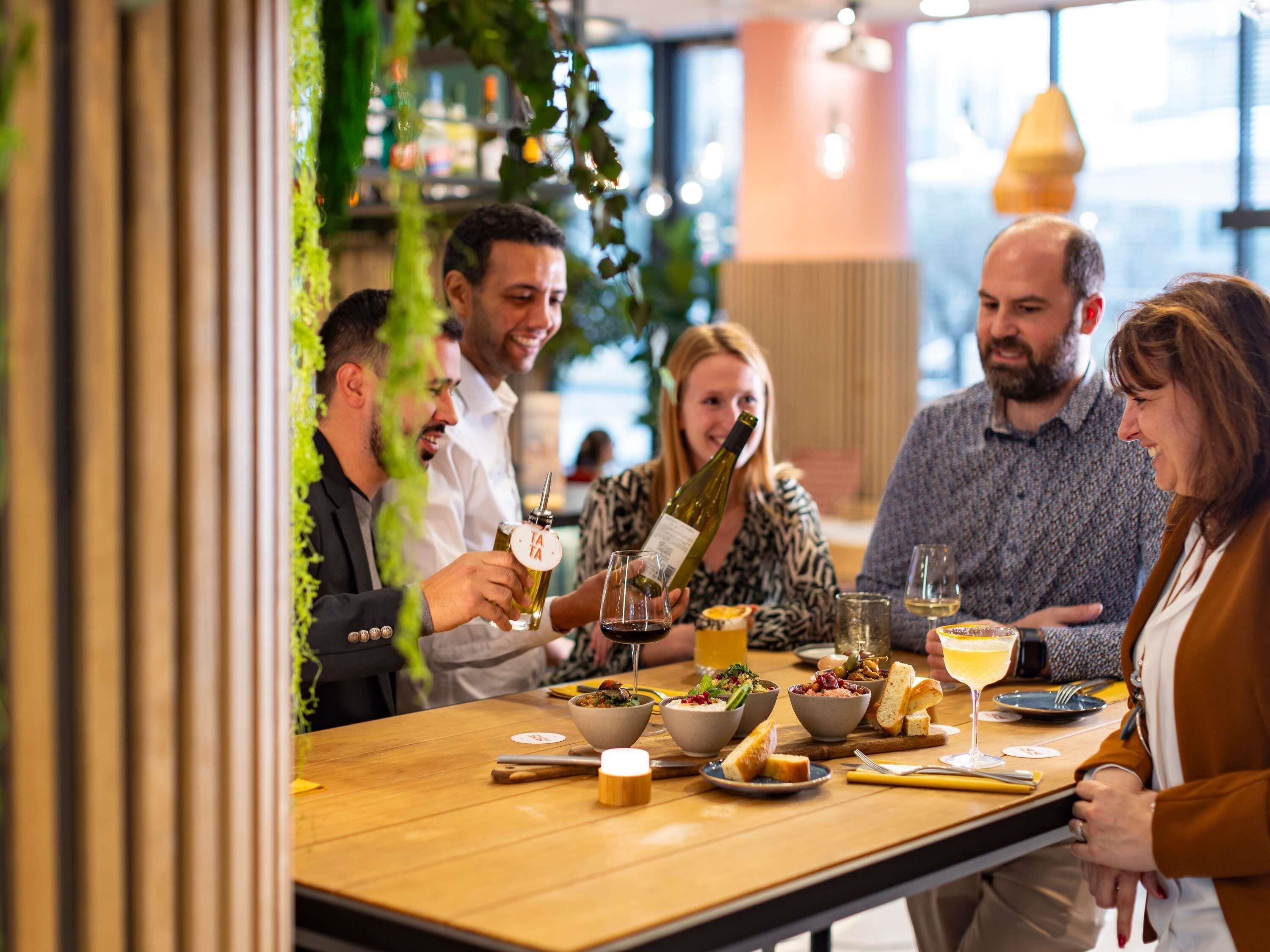 A group of people dining at a restaurant with a wooden table, various dishes, and drinks.