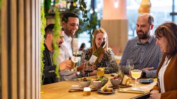 A group of people dining at a restaurant with a wooden table, various dishes, and drinks.