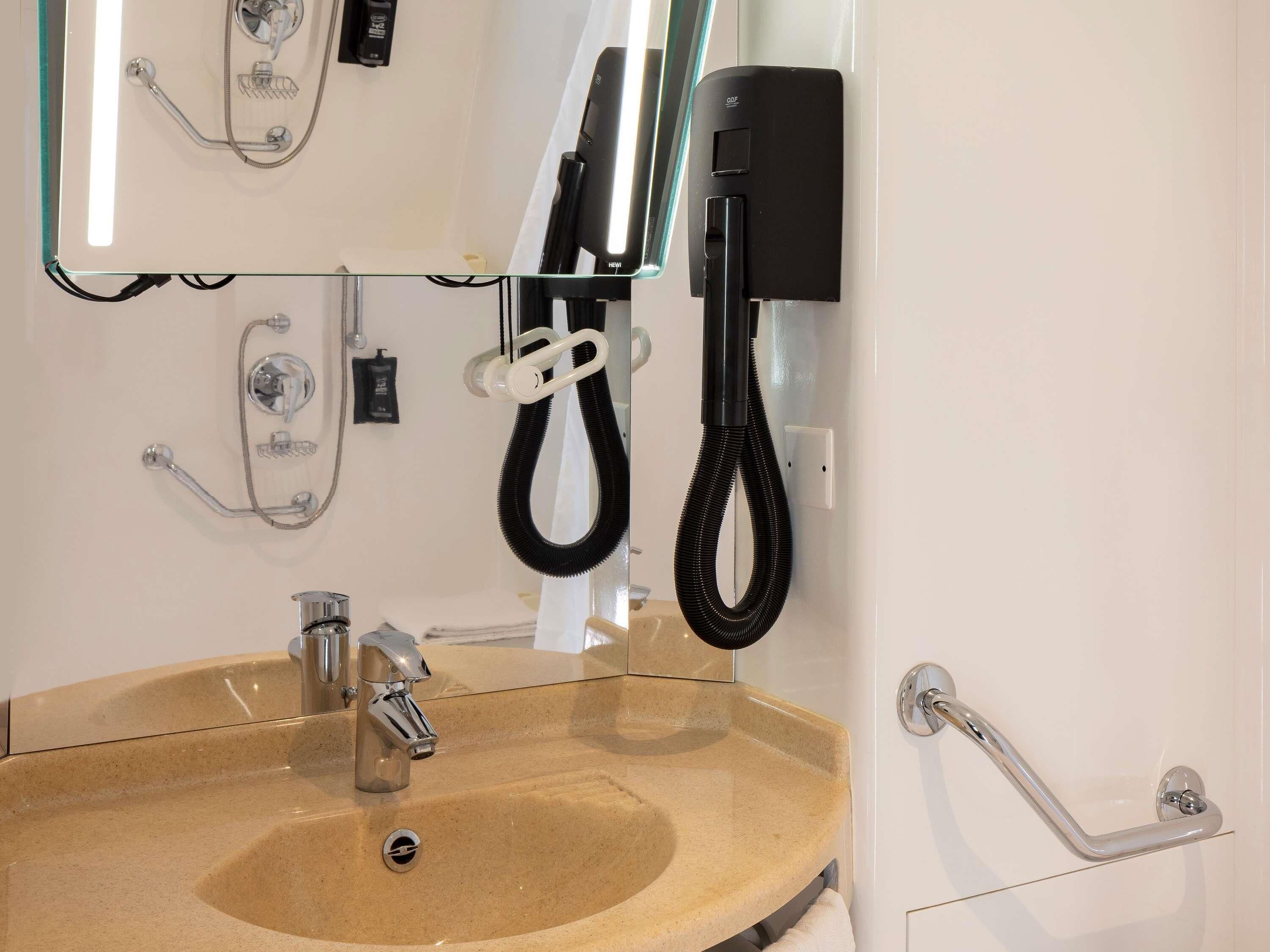 A bathroom with a beige sink, a handheld showerhead, a handheld vacuum cleaner, and a wall-mounted telephone.