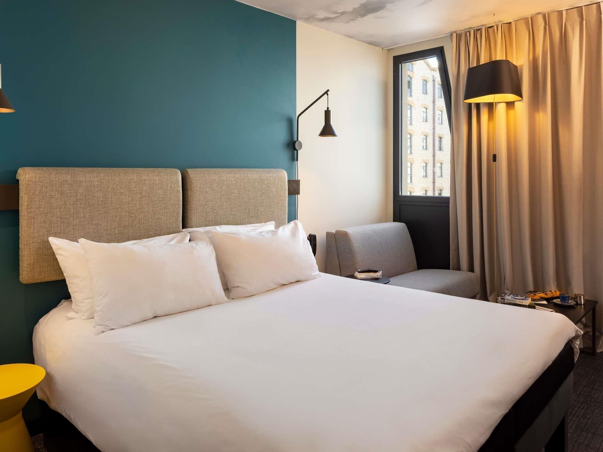 A hotel room with a large bed, a chair, a desk, a lamp, and a window with curtains.