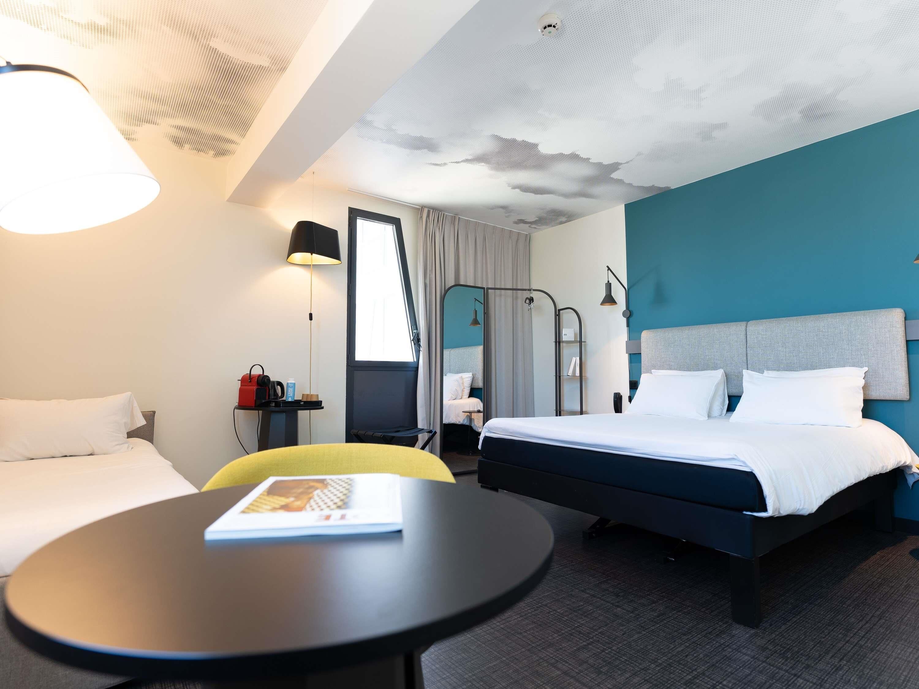 Une chambre d’hôtel comprenant un lit, un bureau, une chaise, une lampe, une fenêtre et un plafond au décor texturé.
