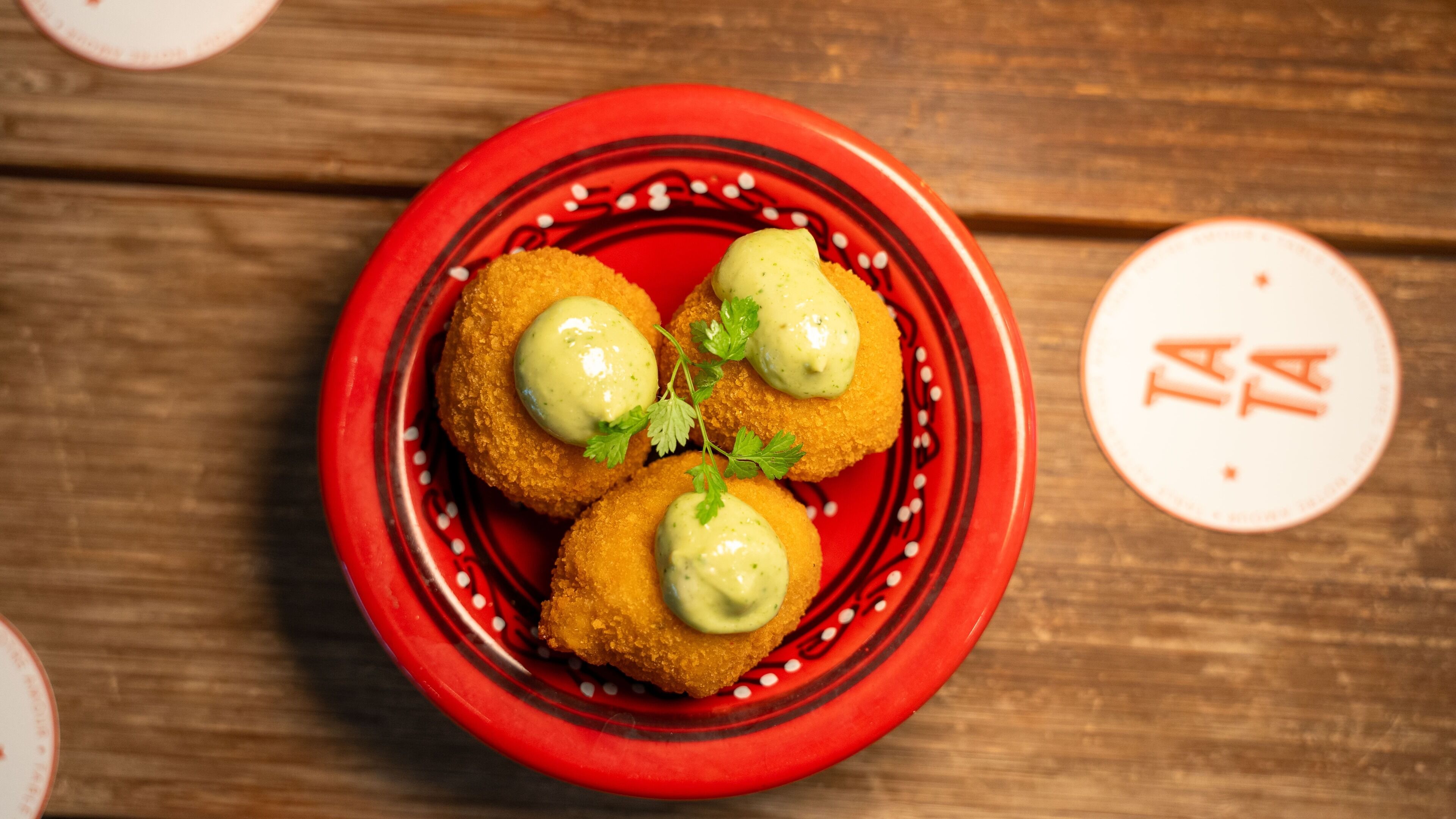 A red plate with three breaded items topped with green sauce and parsley, on a wooden table.