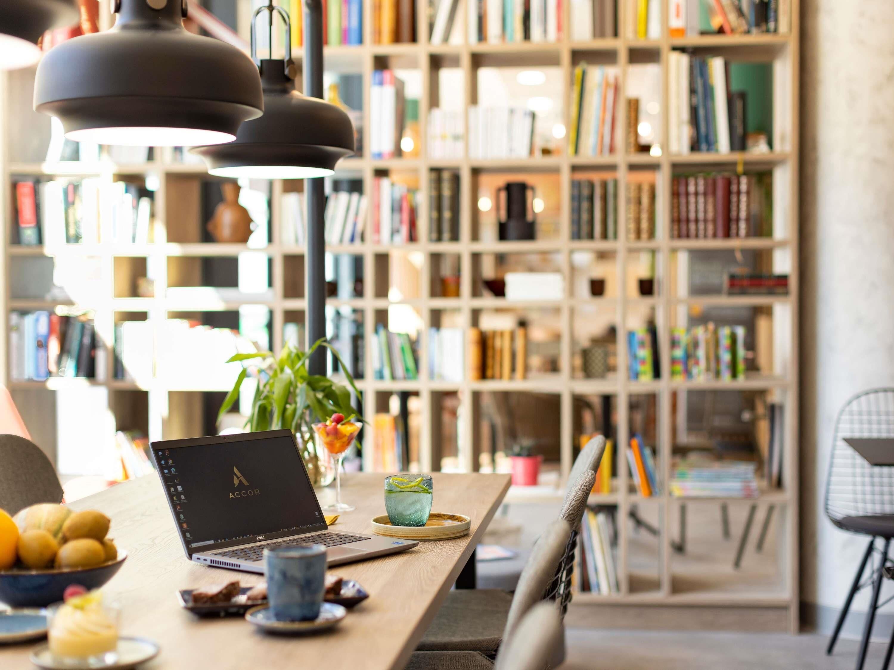 A cozy workspace with a laptop, a bowl of fruit, a glass of drink, and a bookshelf filled with books.