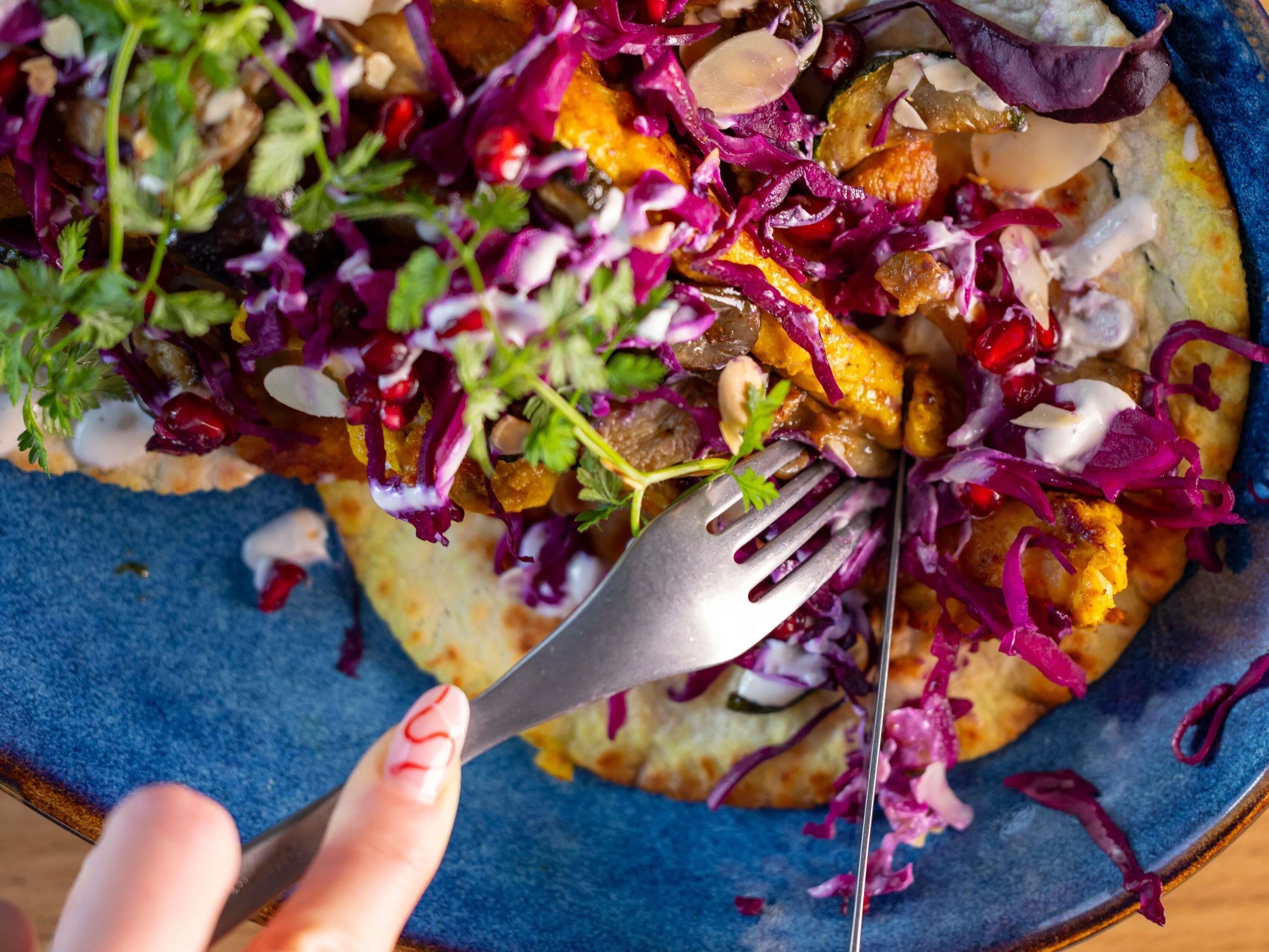 Primer plano de un plato colorido con un tenedor, con verduras vibrantes y salsa cremosa.