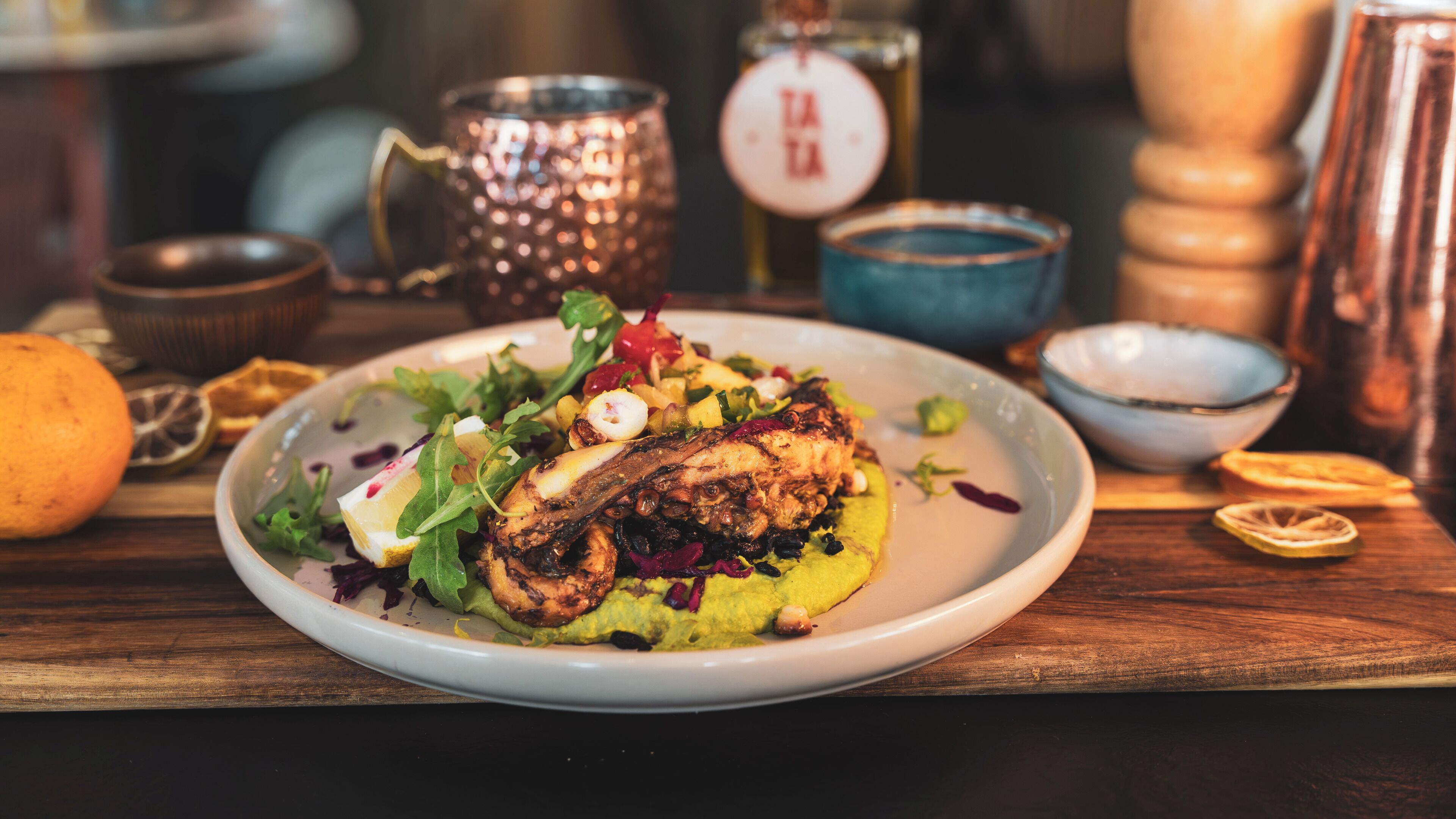 A plate of food with a variety of vegetables and a piece of grilled meat, accompanied by a lemon wedge and a bowl of dressing.