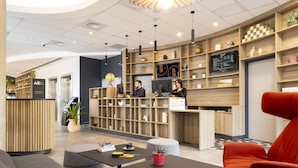 Una moderna zona de recepción con estanterías de madera, un mostrador de recepción y un área de descanso con una silla roja.