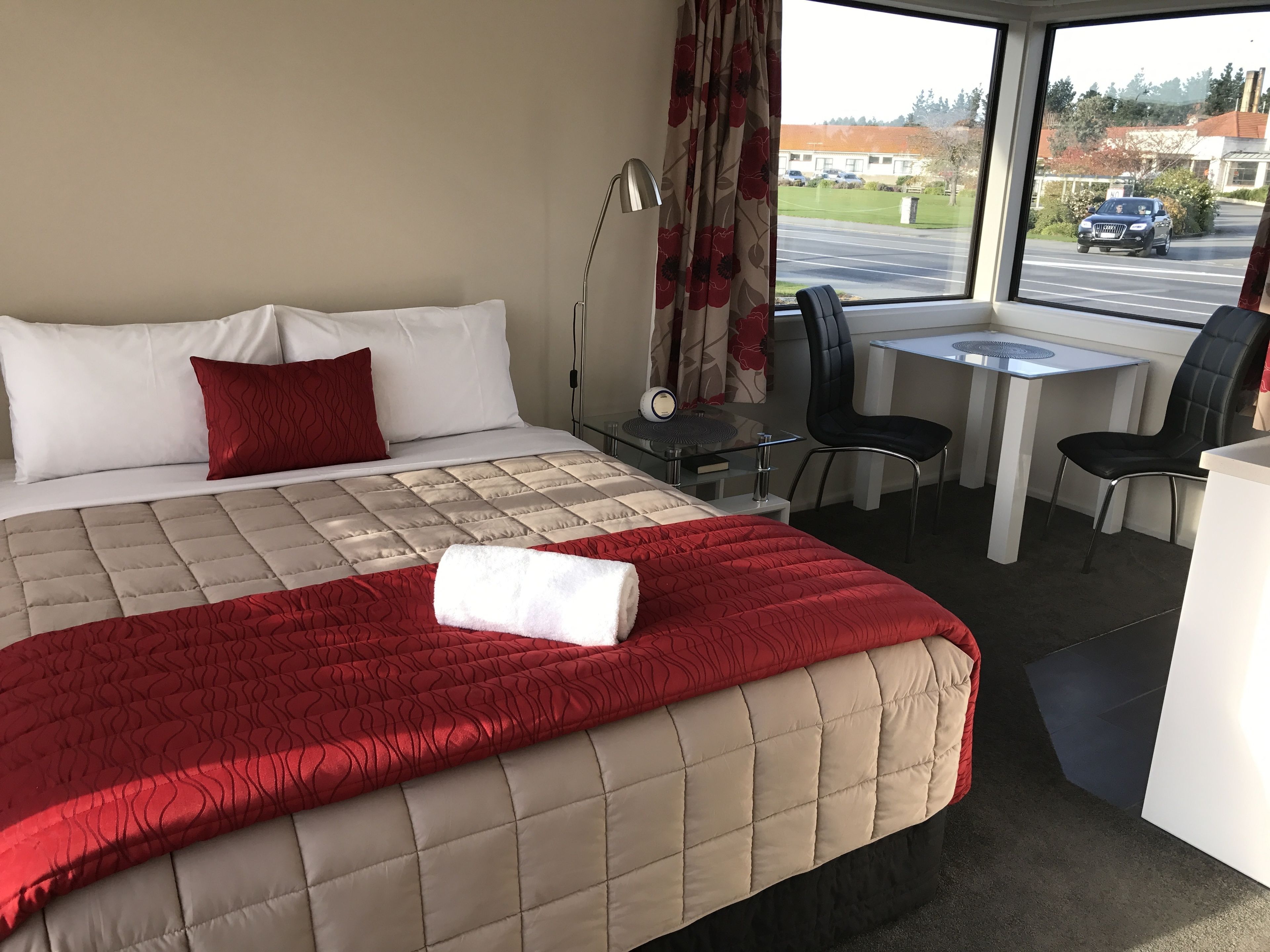 A hotel room with a bed, a desk, a chair, and a view of the street outside.