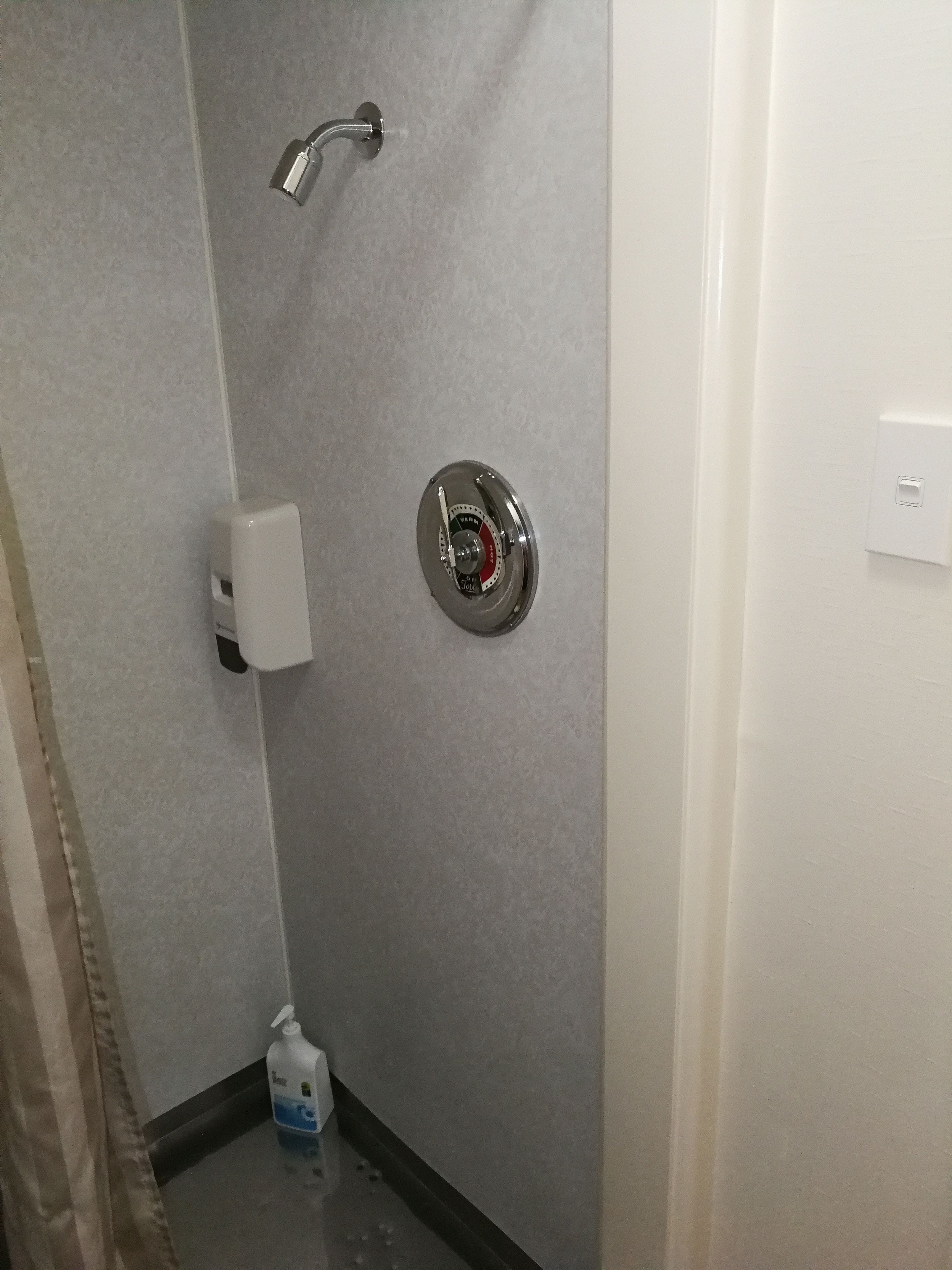 Une salle de bain équipée d’une douche, d’un distributeur de savon et d’un sèche-mains.
