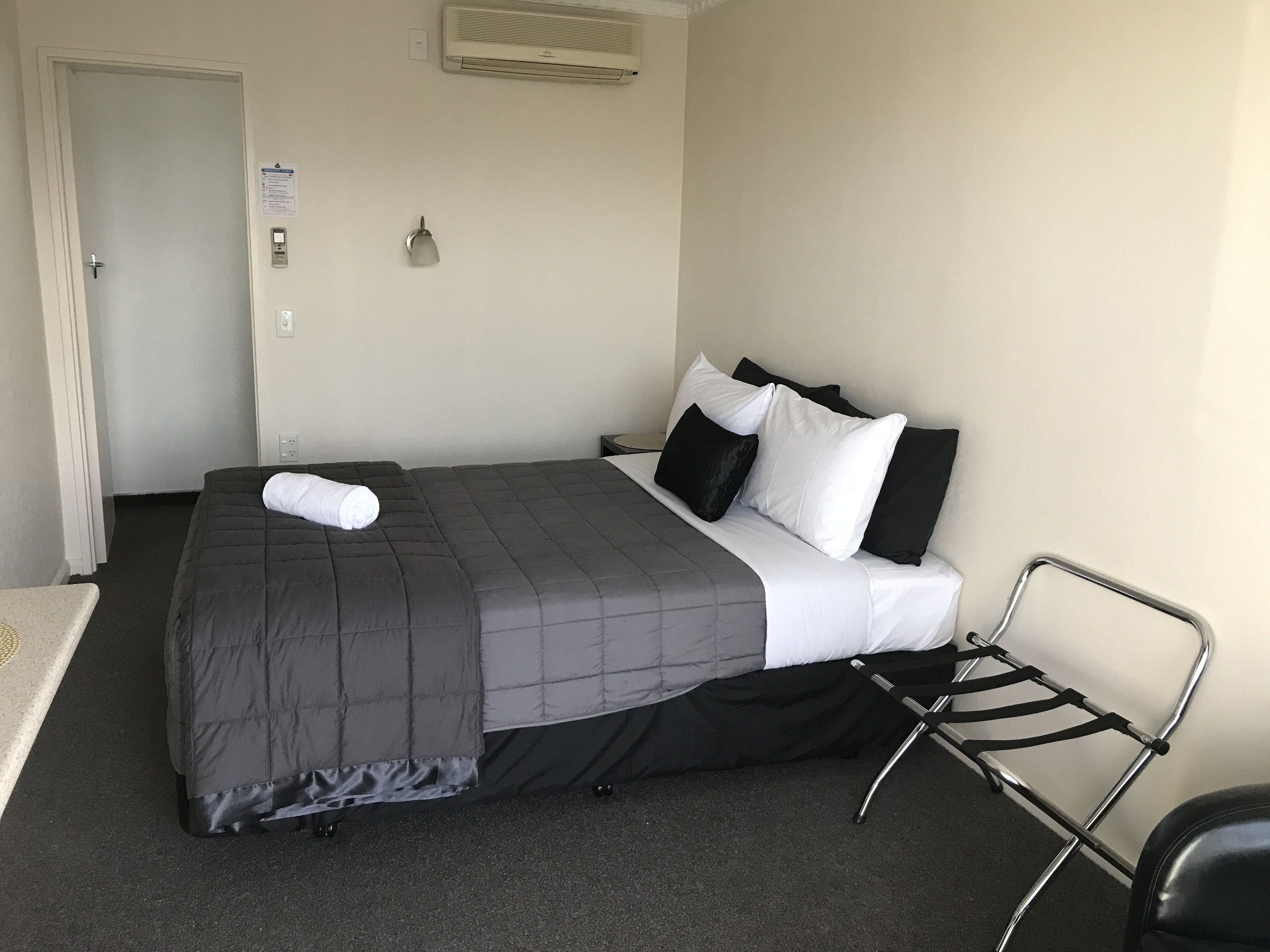 Une chambre d’hôtel avec un lit, une chaise, un climatiseur fixé au mur et une porte.