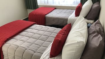 Two beds with red and white bedding, a window with curtains, and a city view.