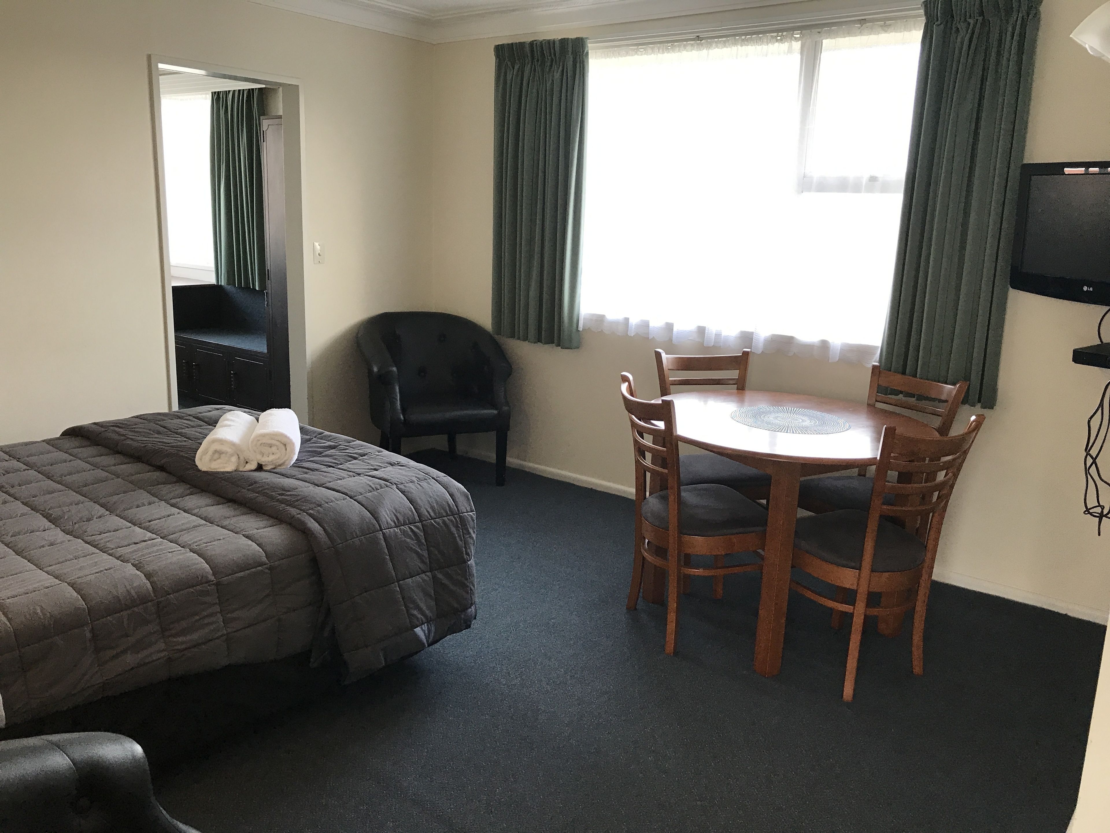 Una habitación de hotel con cama, una mesa con sillas, televisor y ventana con cortinas.