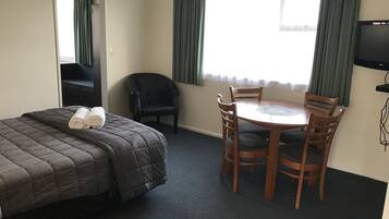 Una habitación de hotel con cama, una mesa con sillas, televisor y ventana con cortinas.