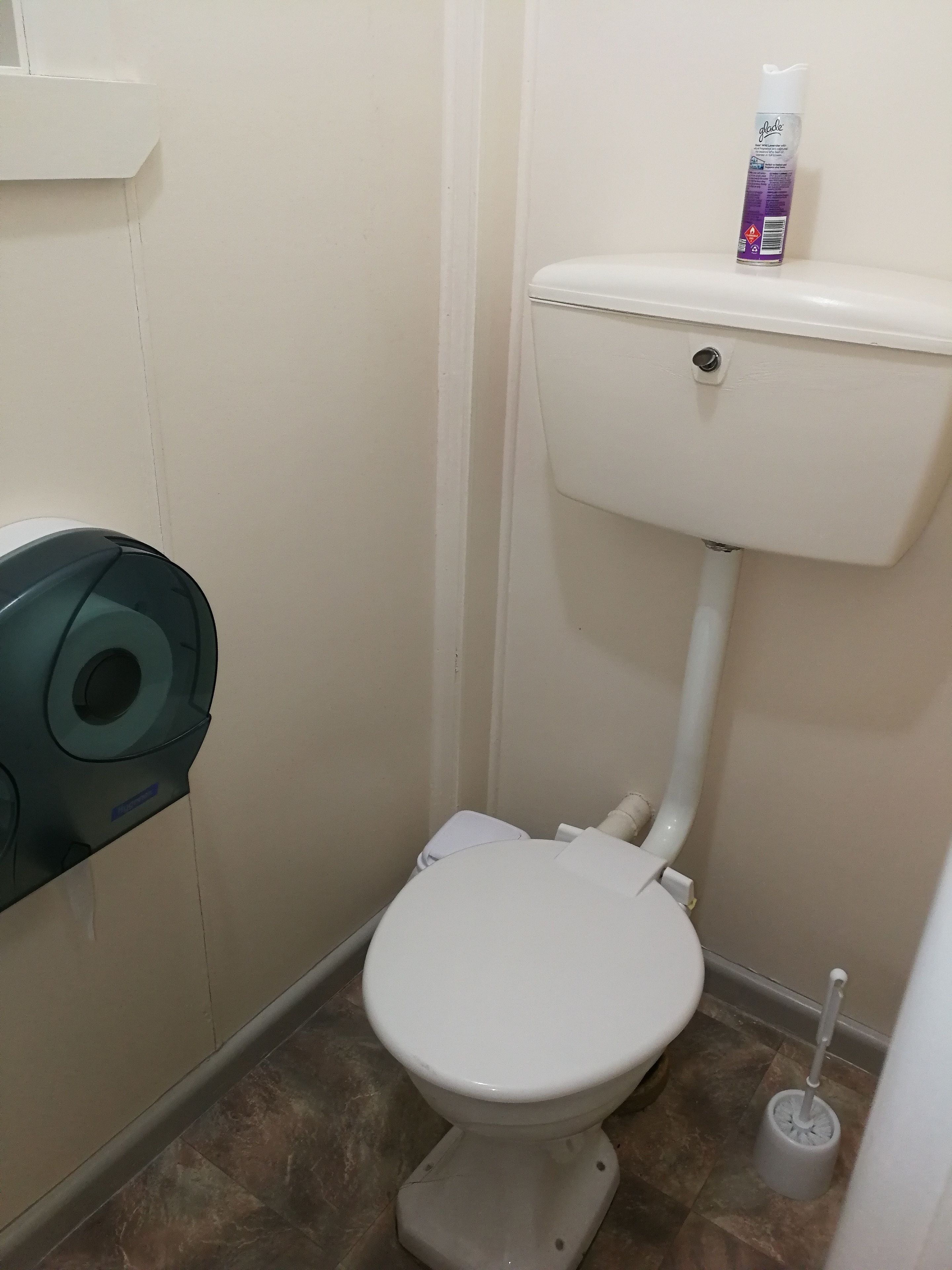 Un baño pequeño y funcional con inodoro, dispensador de papel higiénico y un desatascador en el suelo.