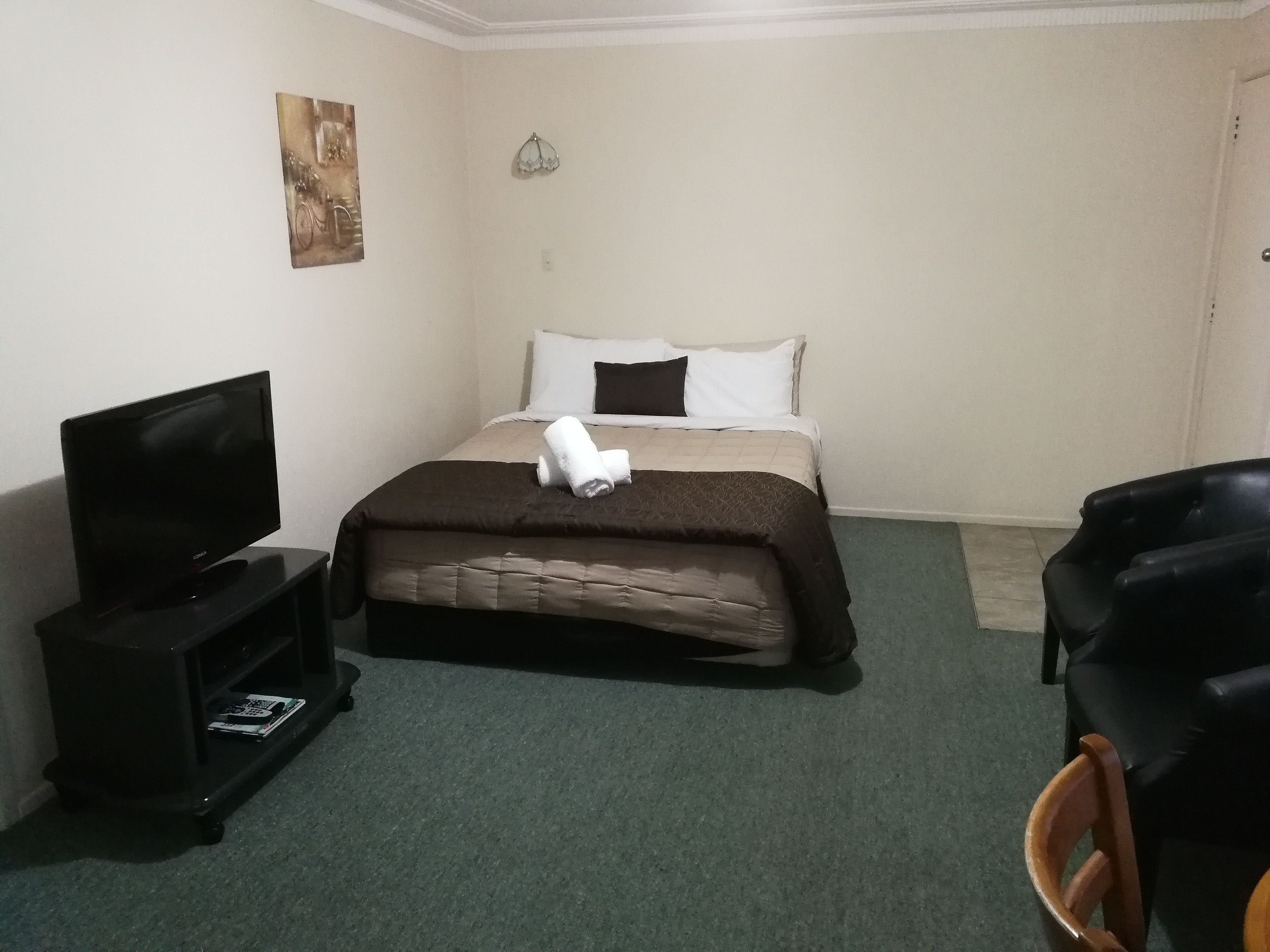 A hotel room with a bed, a TV on a stand, a chair, and a small table.