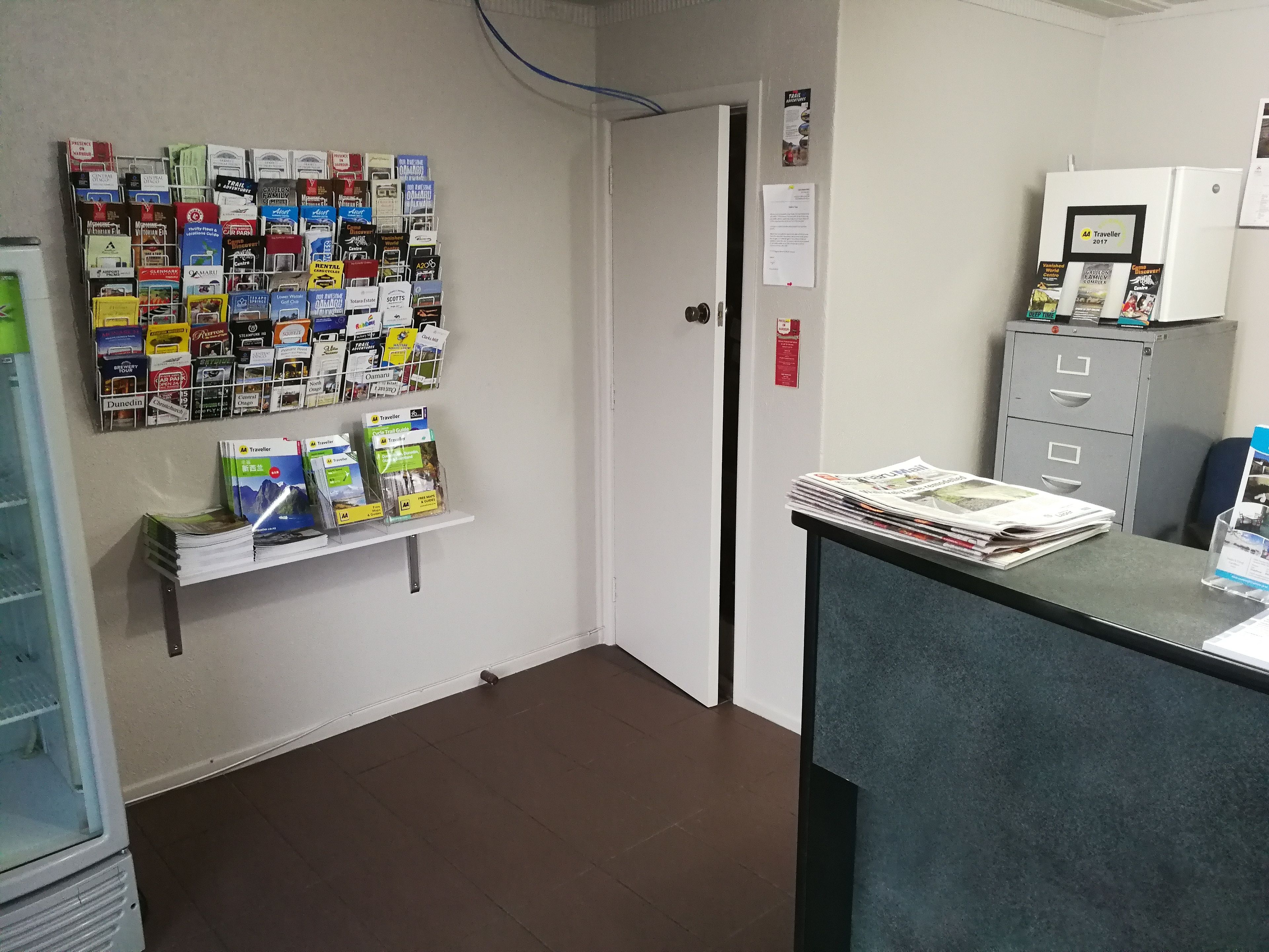 A reception area with a bulletin board displaying various travel guides, a counter with newspapers, and a filing cabinet.