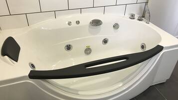Una bañera blanca con una barra de seguridad negra, grifería de cromo y una pared con azulejos al fondo.