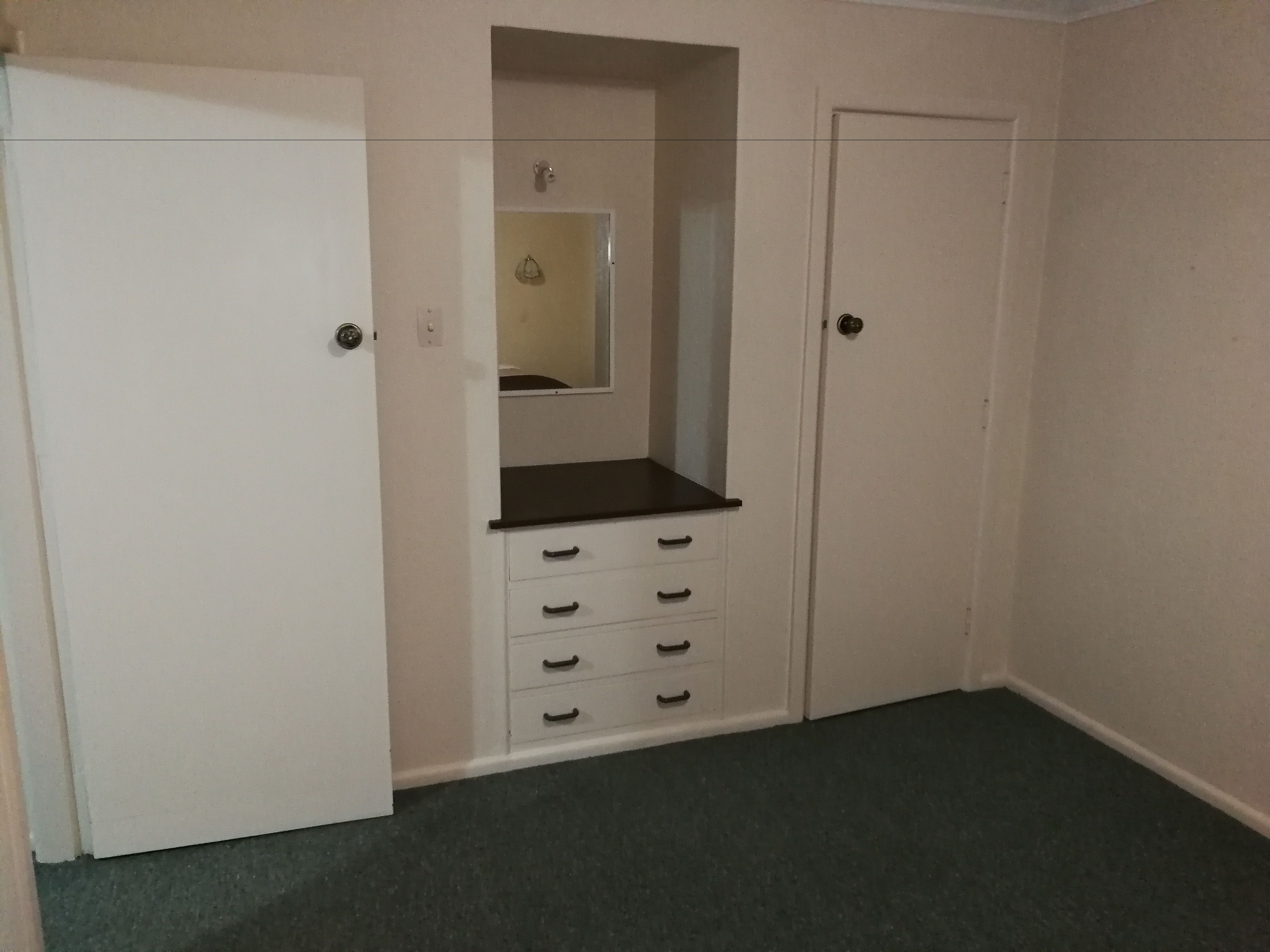 Una habitación pequeña y cerrada con una puerta blanca, un espejo y una encimera negra con cajones.