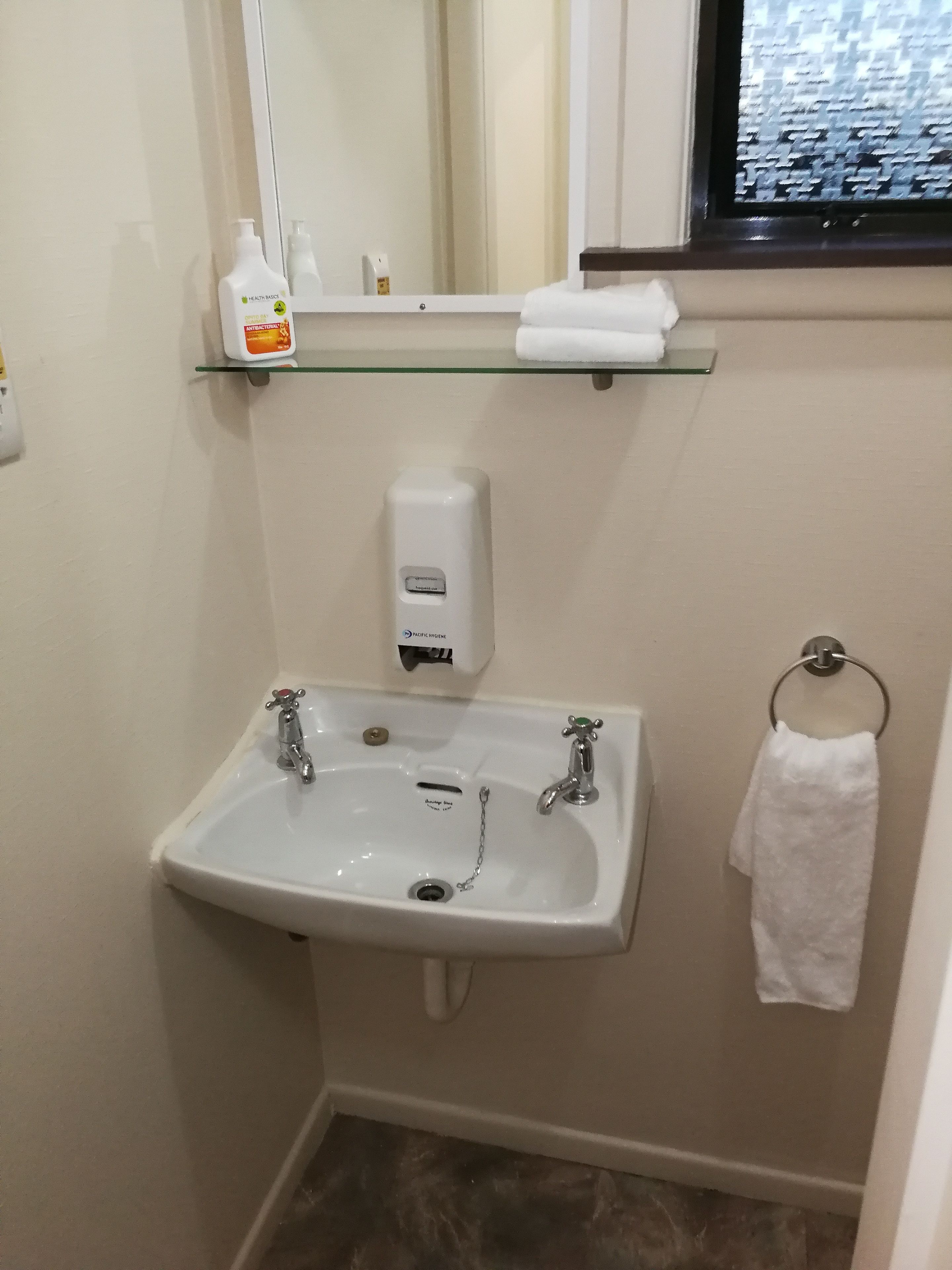 A bathroom with a white sink, a mirror, a glass shelf with toiletries, and a towel rack.