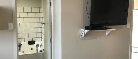 A bathroom with a tiled wall, a bathtub, and a mounted television on a shelf.