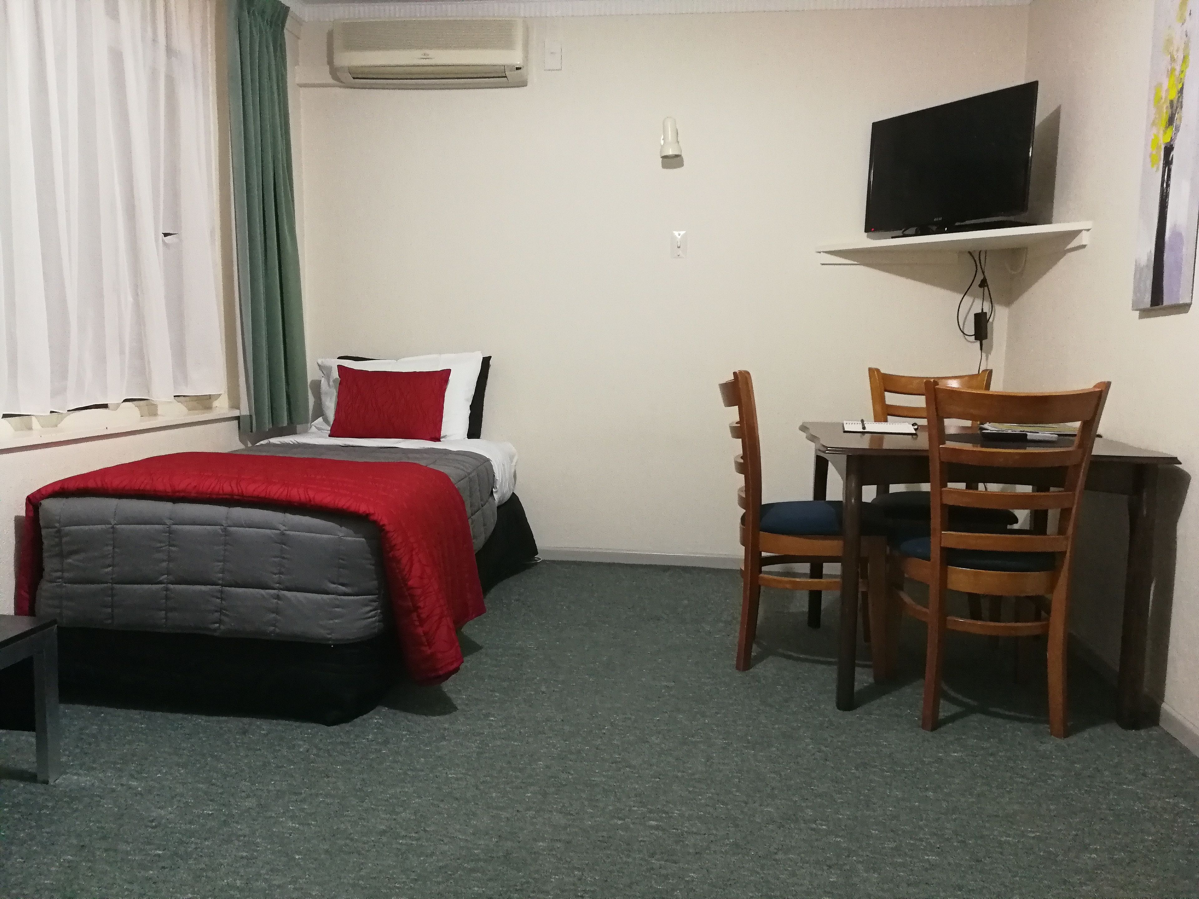 A hotel room with a bed, a desk, a chair, a television, and an air conditioning unit.