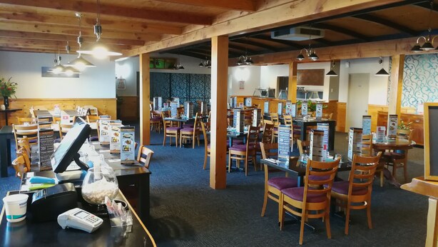 A restaurant with wooden beams, tables, chairs, and menu boards. - Ascot Oamaru Motel (Oamaru)