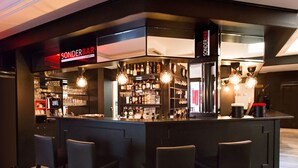 A bar area with a black counter, bar stools, and shelves stocked with bottles and glasses.