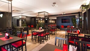 A modern restaurant with black and red furnishings, a bar area, and a large mirror reflecting the space.