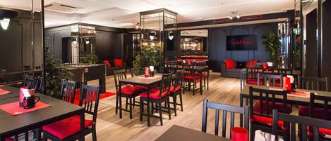 A modern restaurant with black and red furnishings, a bar area, and a large mirror reflecting the space.