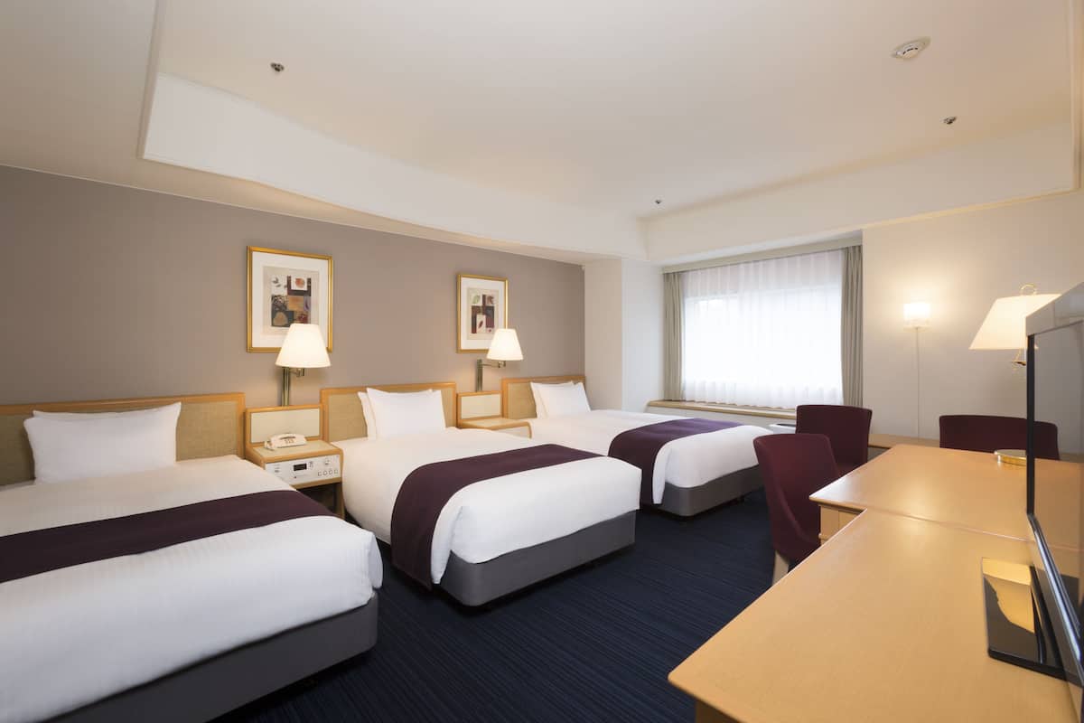 Une chambre d’hôtel avec trois lits, un bureau et une grande fenêtre.
