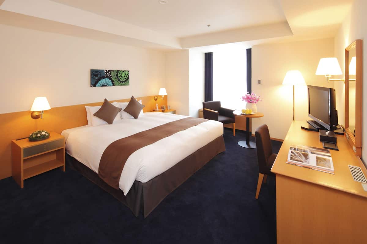 Une chambre d’hôtel avec un grand lit, des lampes de chevet, un bureau avec un ordinateur, une chaise et un téléviseur.