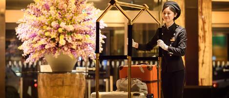 A hotel lobby with a large floral arrangement, a luggage cart, and a person in uniform.