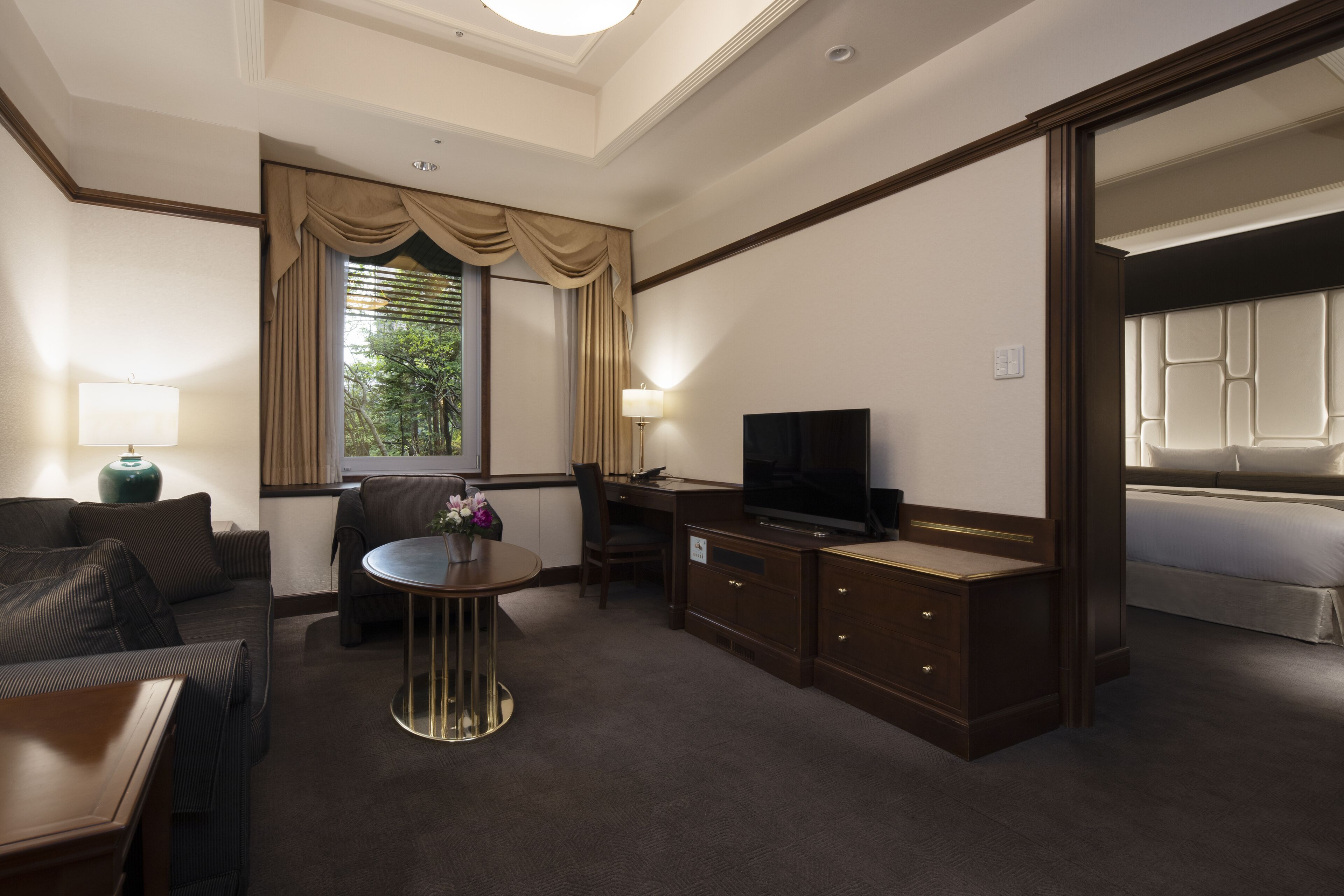 A hotel room with a sofa, a dining table with chairs, a TV, a desk, and a bed.