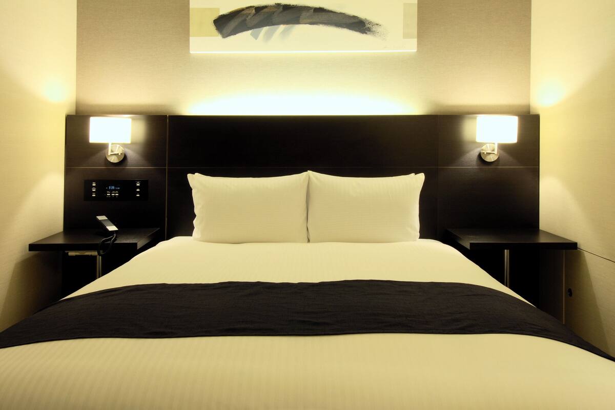 Une chambre d’hôtel avec un grand lit, deux tables de chevet avec des lampes, une horloge et un panneau de commande numérique.