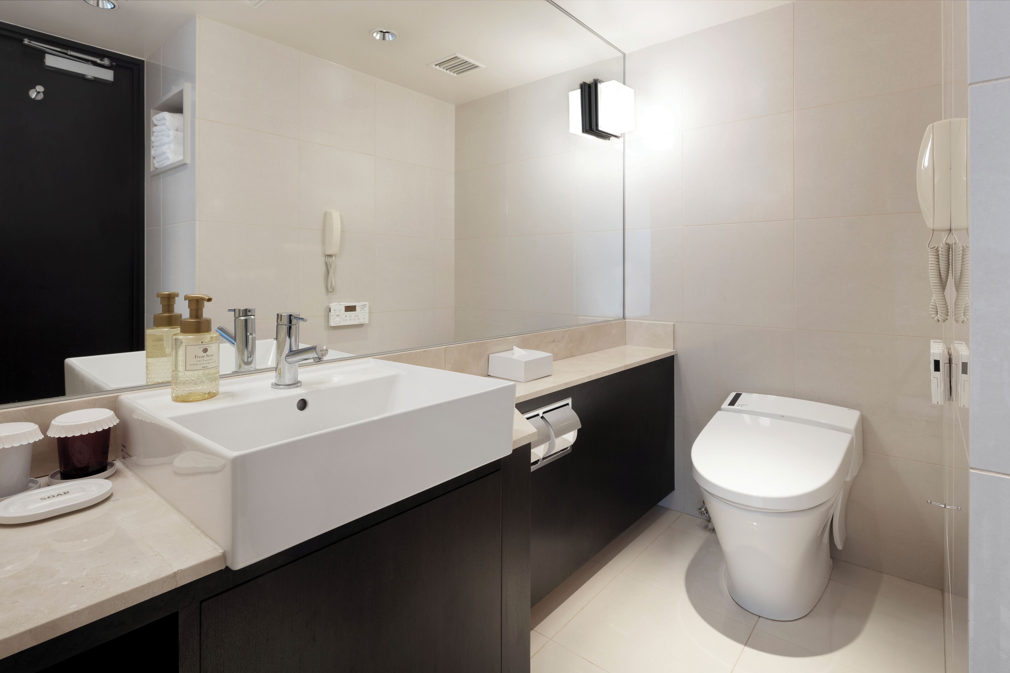 A modern bathroom with a large white sink, dark cabinets, a toilet, and a mirror.