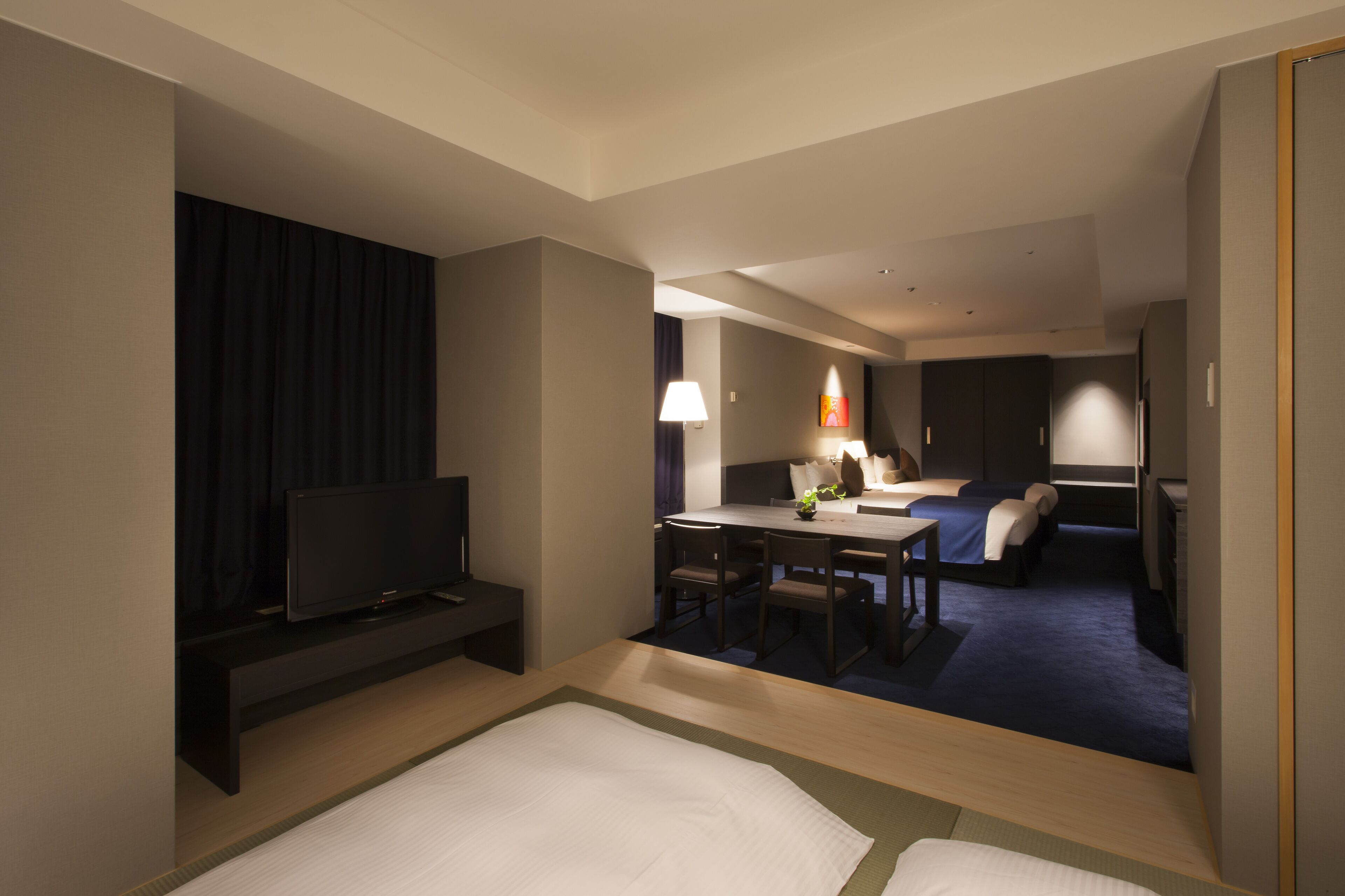 A hotel room with a TV, a dining table, and a bed.