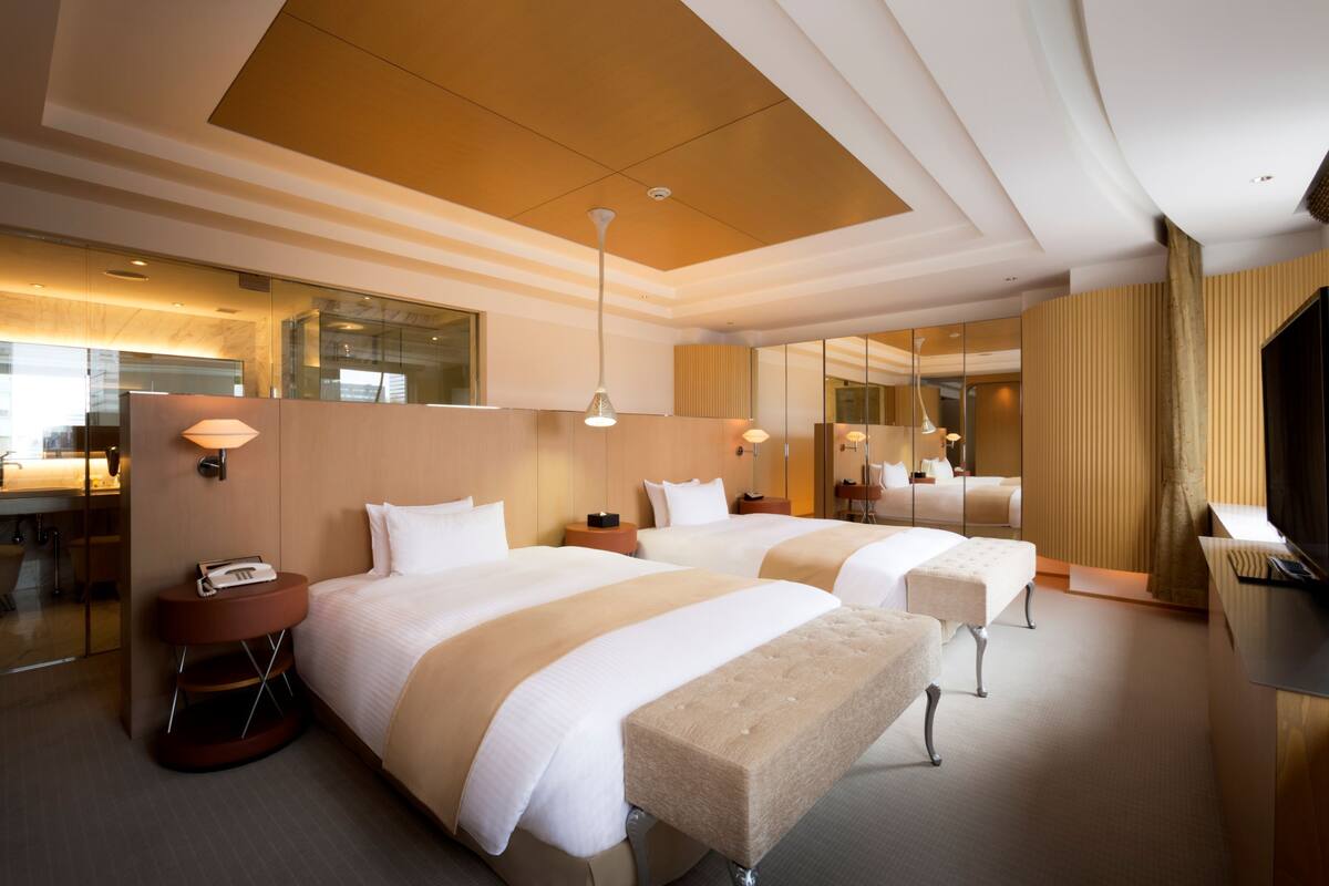 Une chambre d’hôtel avec deux lits, un coin salon, un bureau et un grand miroir.