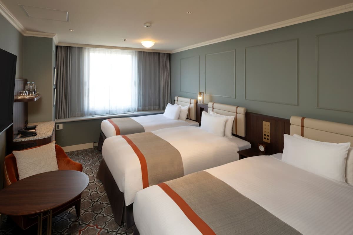 Une chambre d’hôtel avec trois lits, un bureau et une chaise.