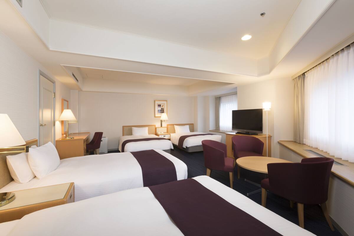 Une chambre d’hôtel avec deux lits, un bureau, une télévision et un coin salon avec des fauteuils.