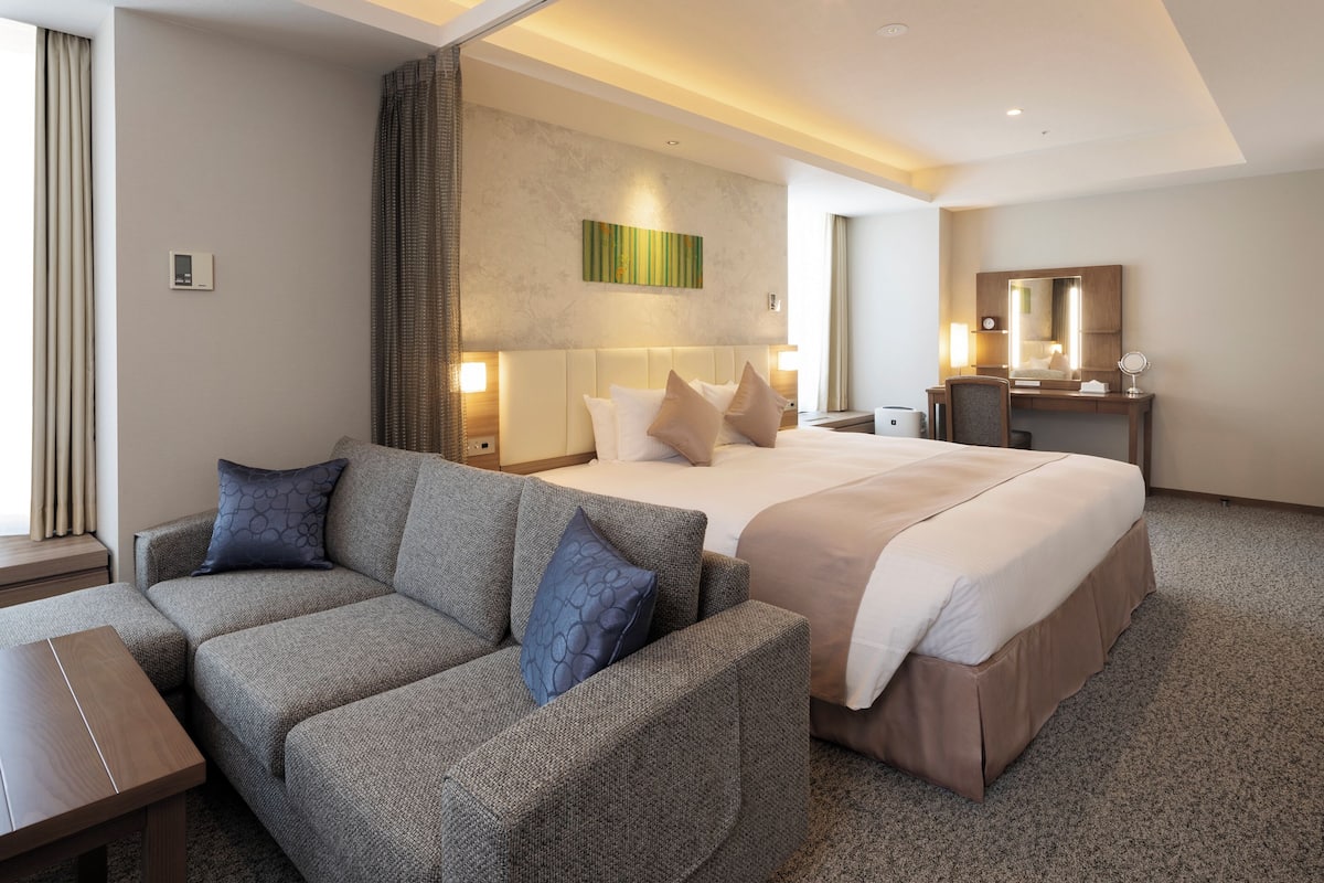 Une chambre d’hôtel moderne avec un grand lit, un canapé, un bureau et un miroir.