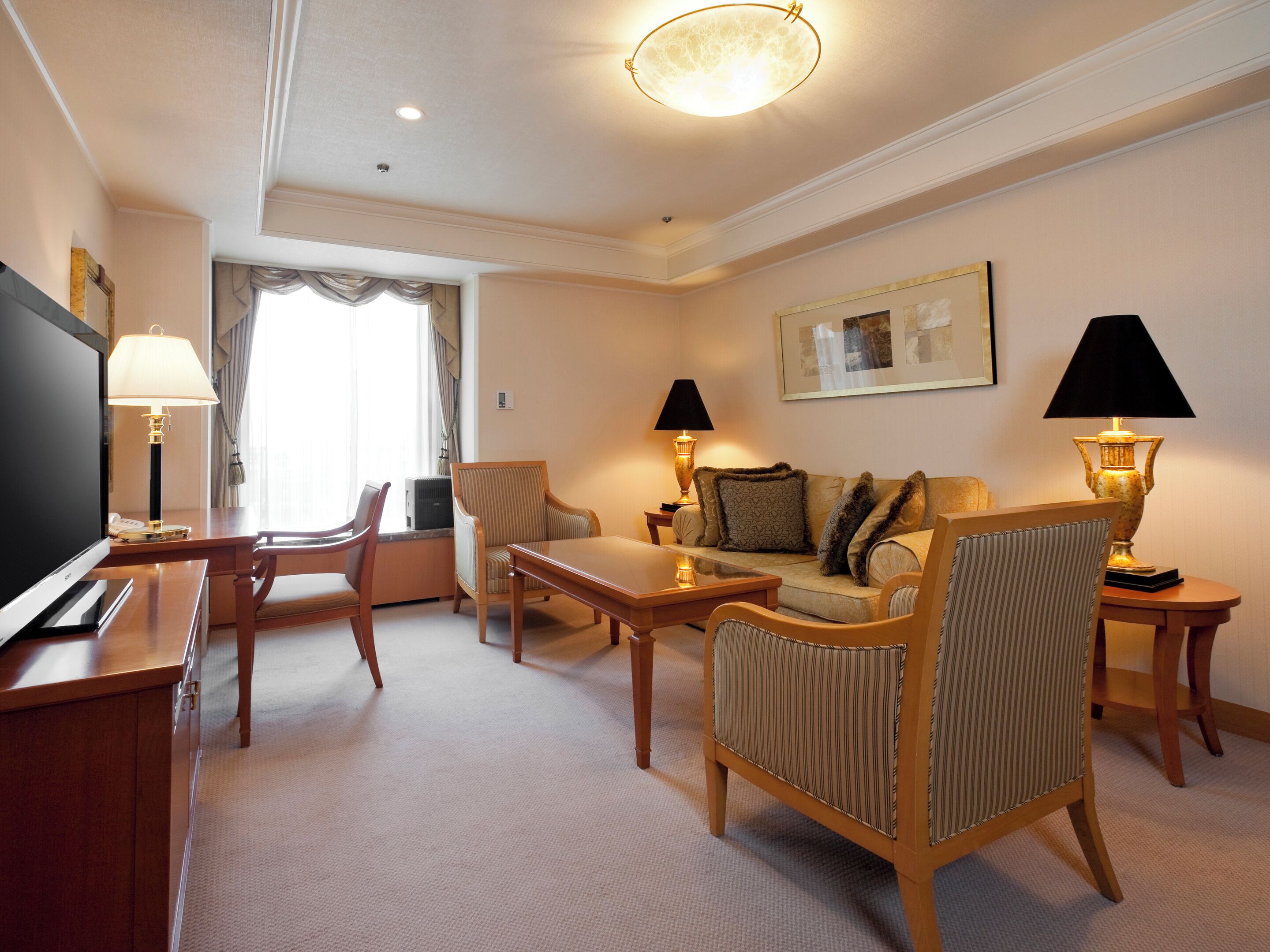 A hotel room with a TV, a sofa, a dining table, and two lamps.