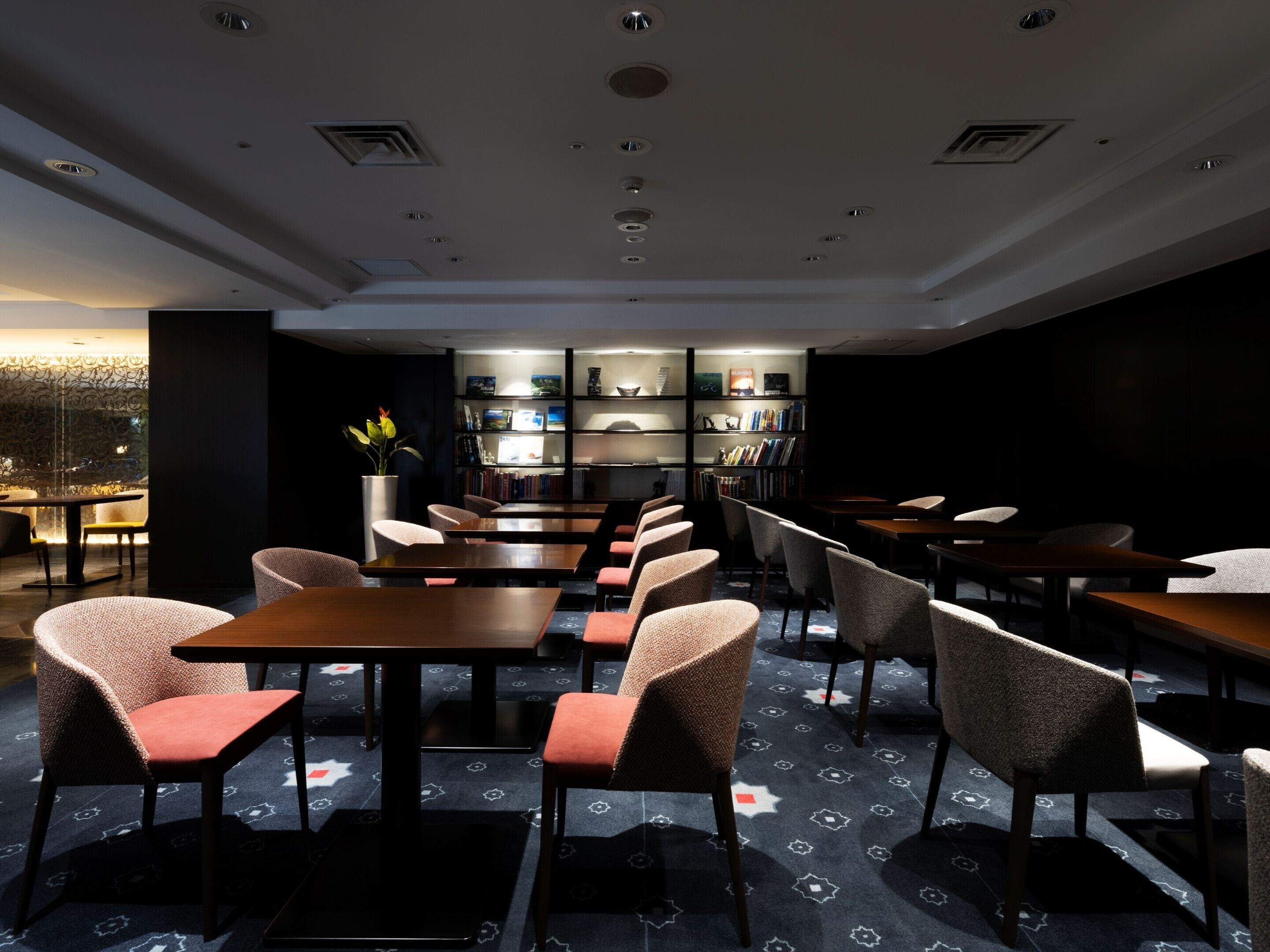 A modern library with bookshelves, tables, and chairs arranged for reading and dining.