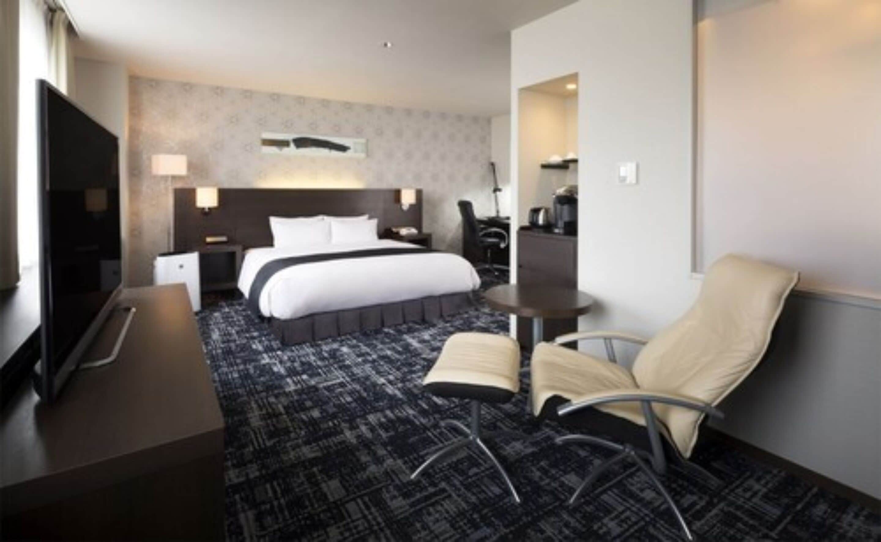 A hotel room with a large bed, a desk, a chair, and a TV.