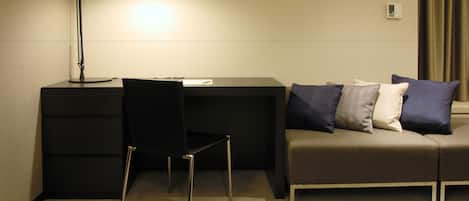 Una habitación de hotel con escritorio, silla y sofá con almohadones.