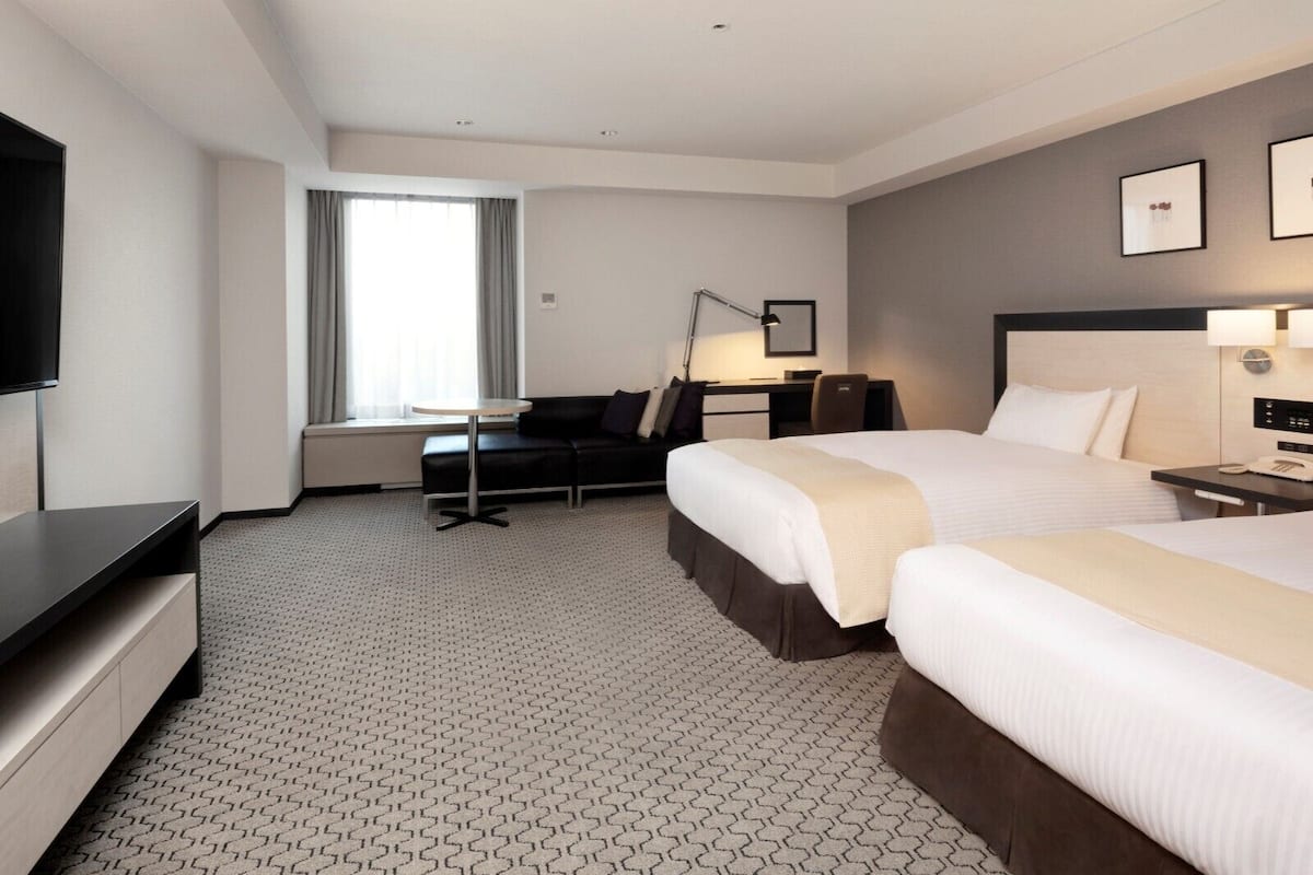 Une chambre d’hôtel avec un grand lit, un bureau avec une chaise, une télévision et une fenêtre avec des rideaux.