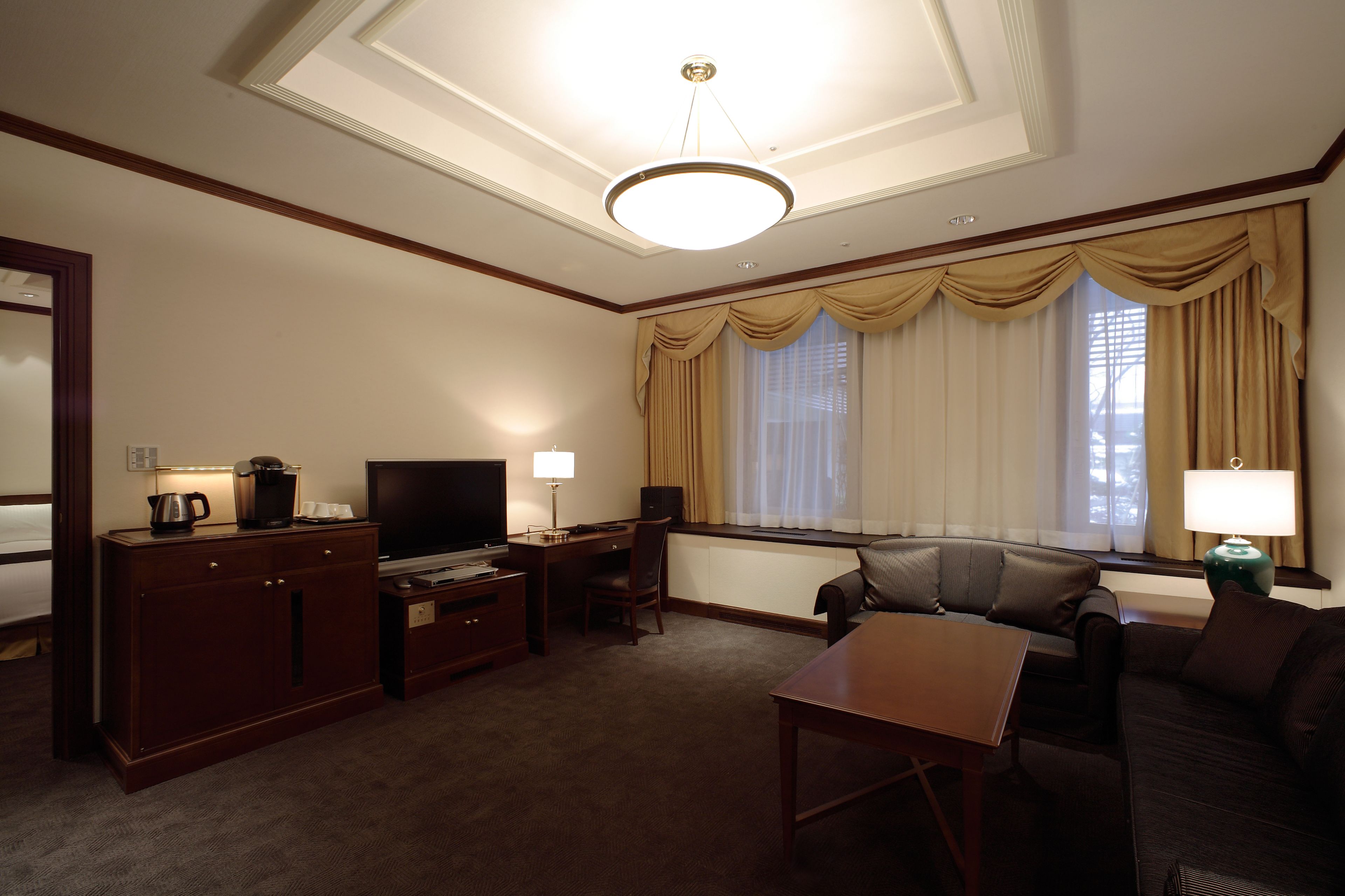 Habitación de hotel con una cama grande, un escritorio con televisor, una silla, un sofá y una ventana con cortinas.
