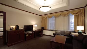 Habitación de hotel con una cama grande, un escritorio con televisor, una silla, un sofá y una ventana con cortinas.